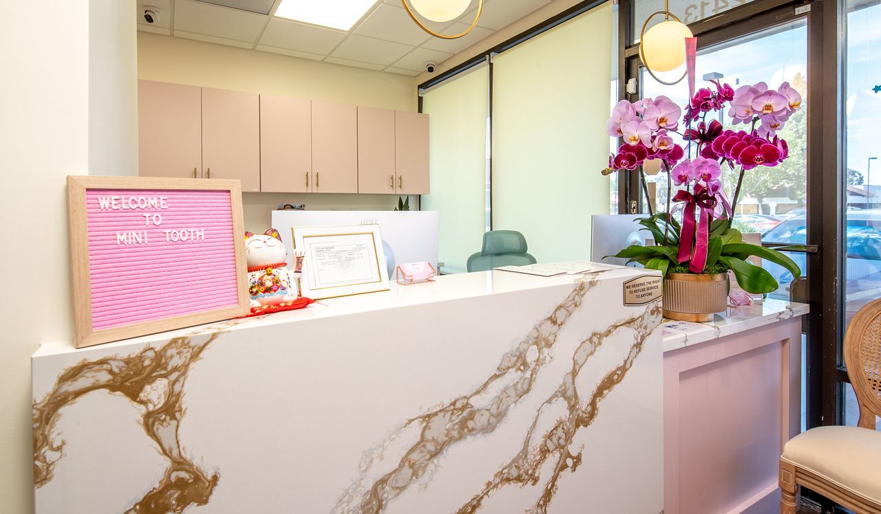 Smiling child in a pink dental chair, wearing a bib, in a pastel-colored dental office.
