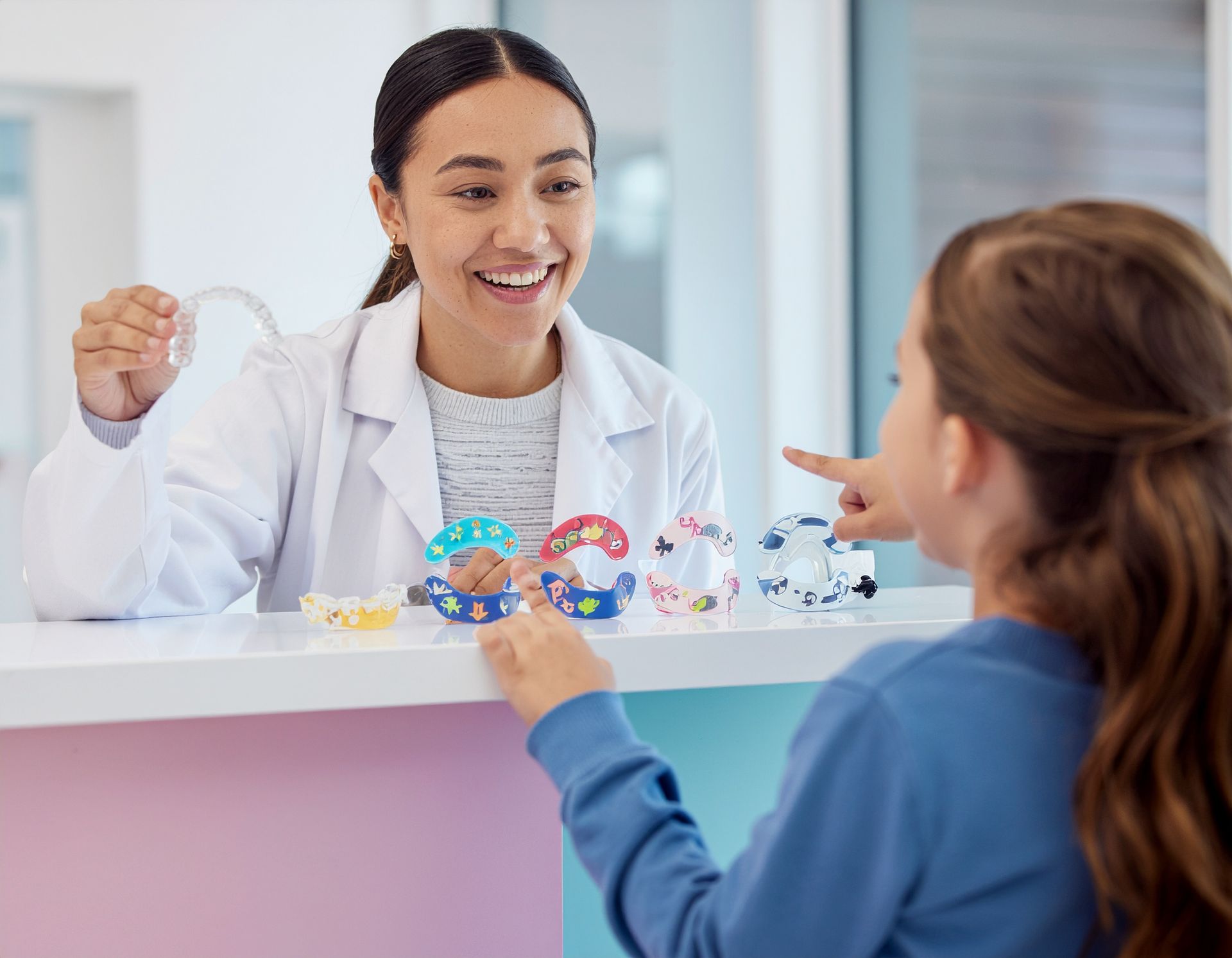 A healthcare professional showing a child colorful mouth guards. The child points to one.