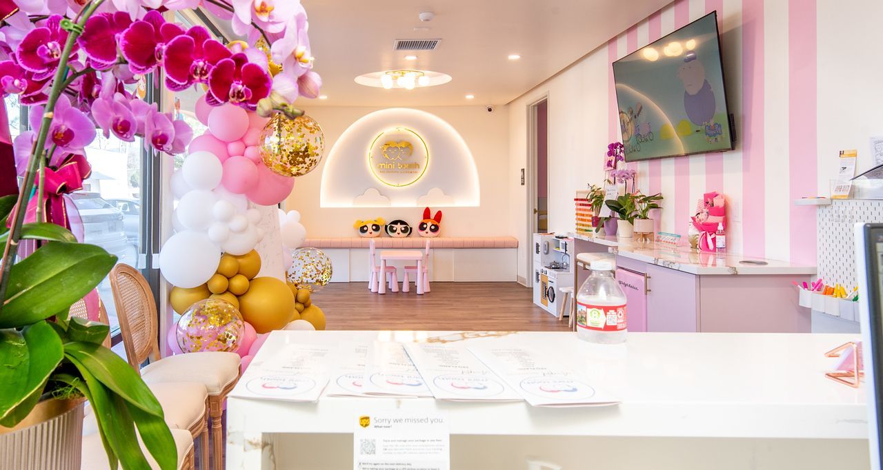 A bright, pastel-colored lobby featuring a white reception desk, pink striped walls, and a floral balloon arch.