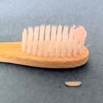 A bamboo toothbrush with pink toothpaste and a detached bristle piece.