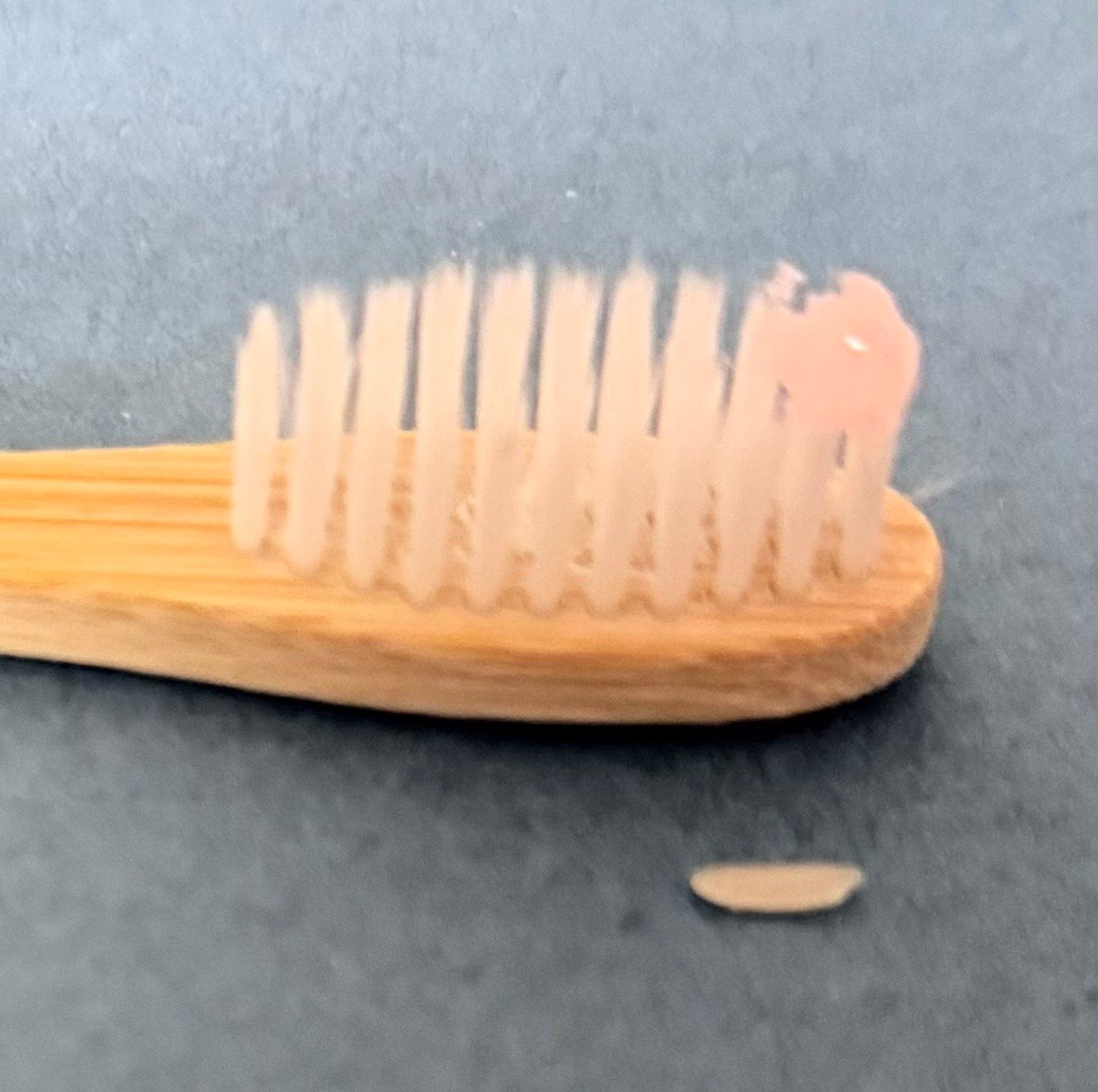 A bamboo toothbrush with pink toothpaste and a detached bristle piece.