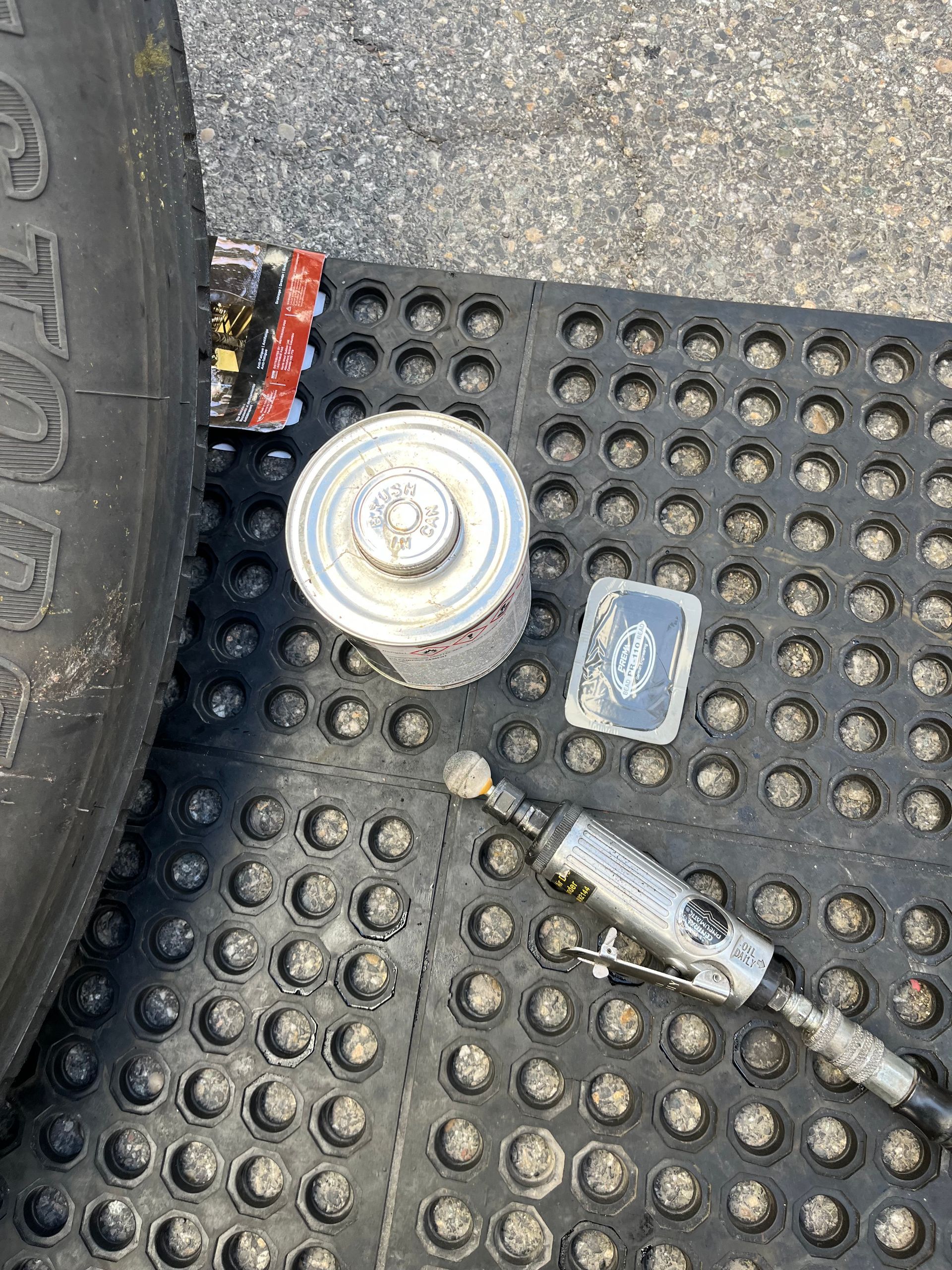 A tire is sitting on top of a black mat next to a can of gas.