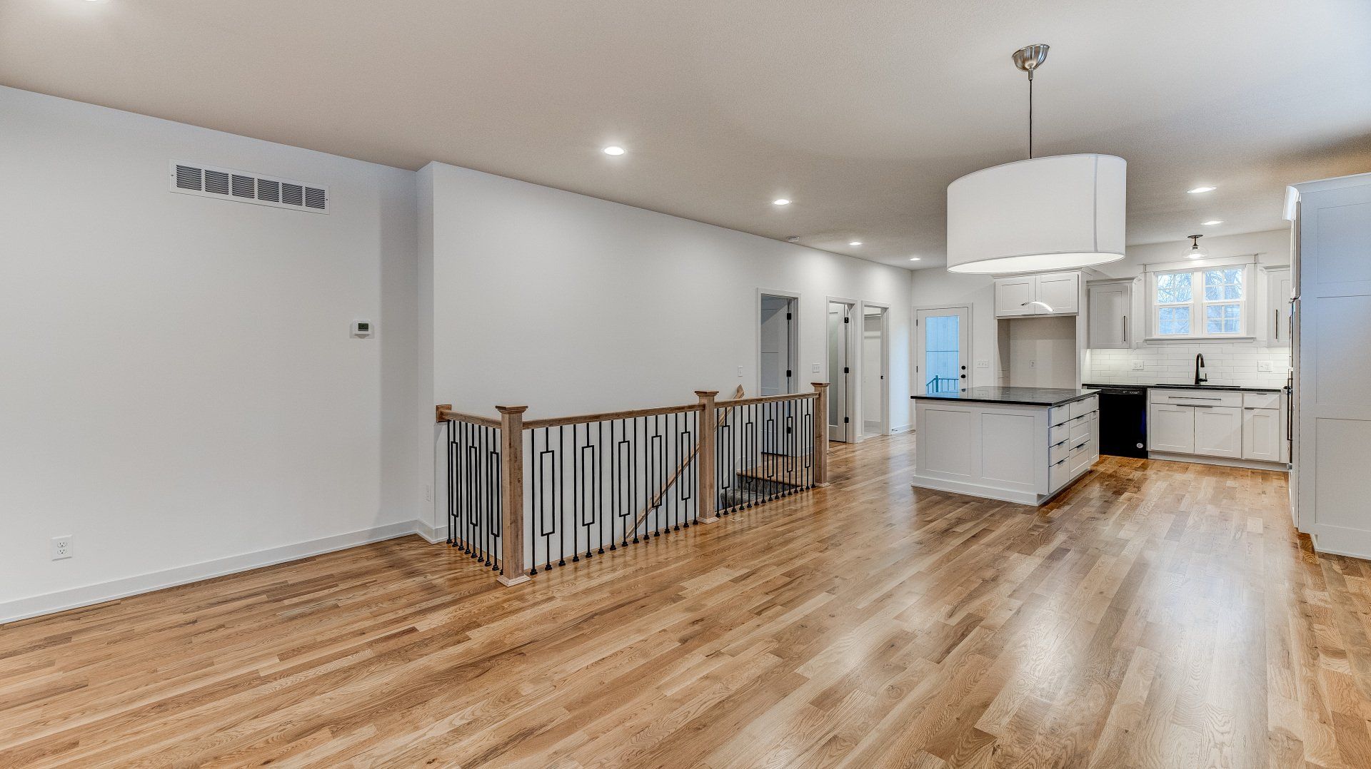 A large empty room with hardwood floors and a kitchen.