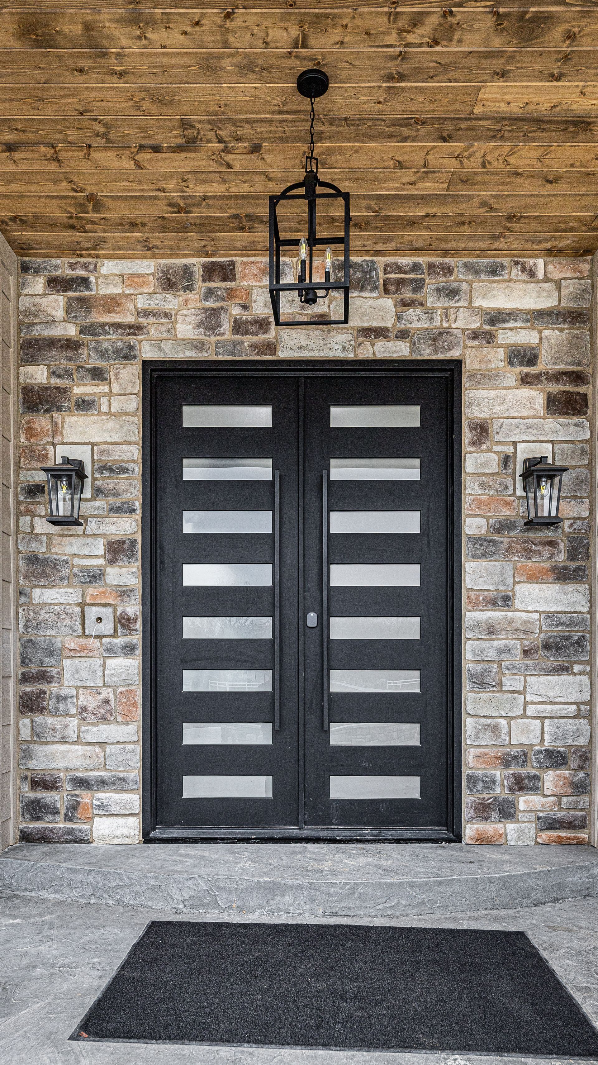 The front door of a brick house with a black door and a lantern hanging from the ceiling.