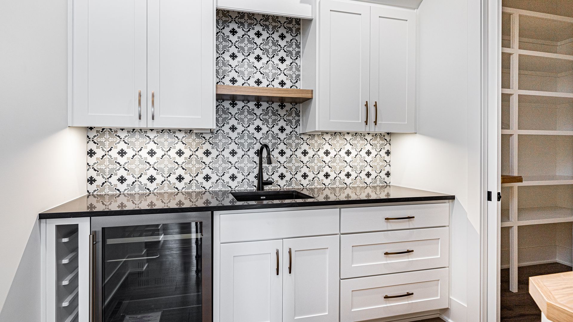 A kitchen with white cabinets , black counter tops , and a wine cooler.