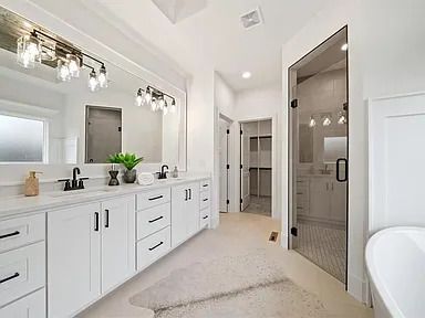 A bathroom with two sinks , two mirrors , a tub and a walk in closet.