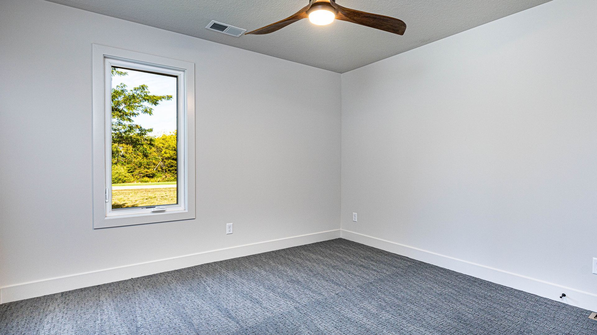 An empty bedroom with a window and a ceiling fan.