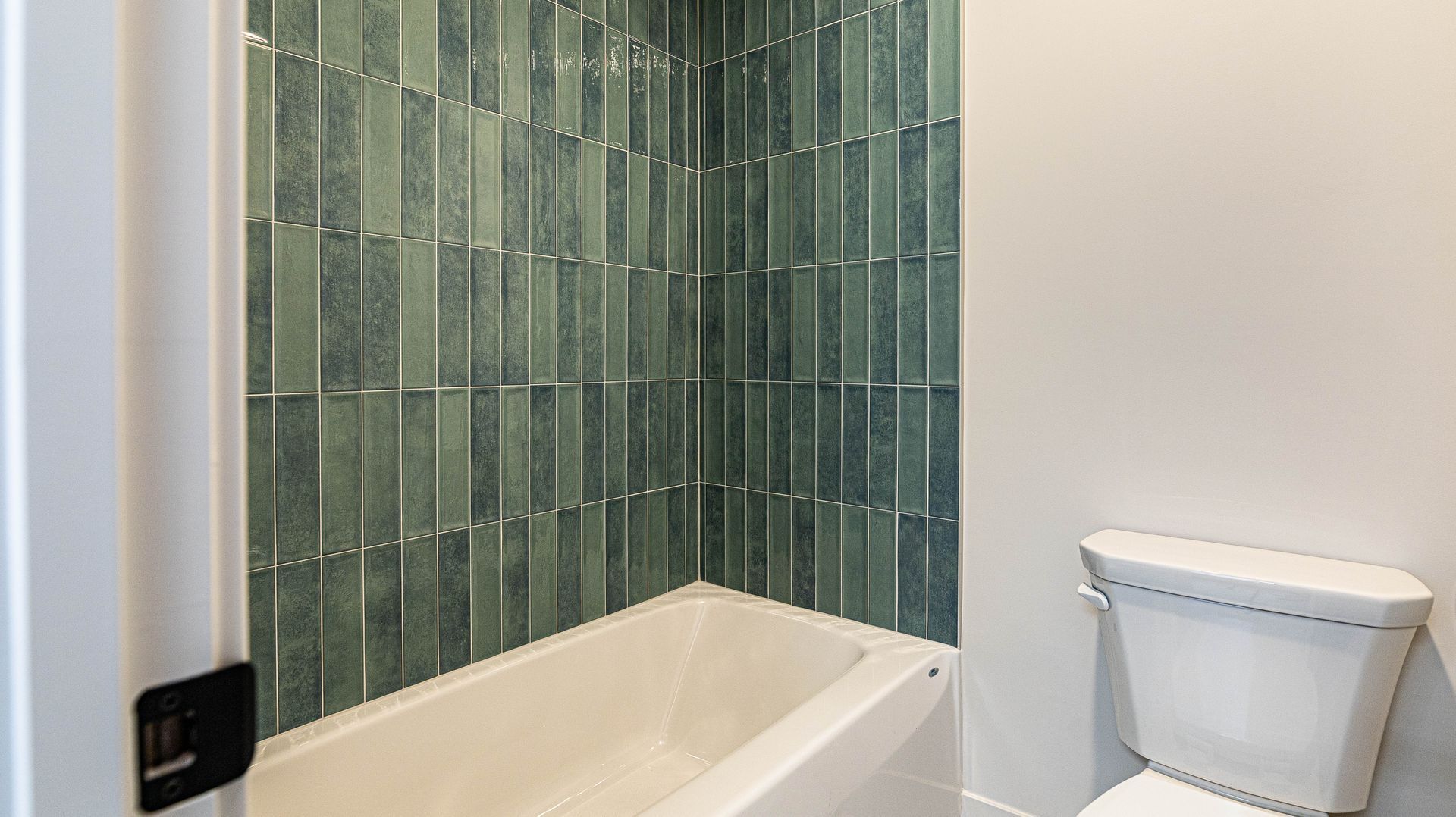 A bathroom with a bathtub , toilet and green tiles.
