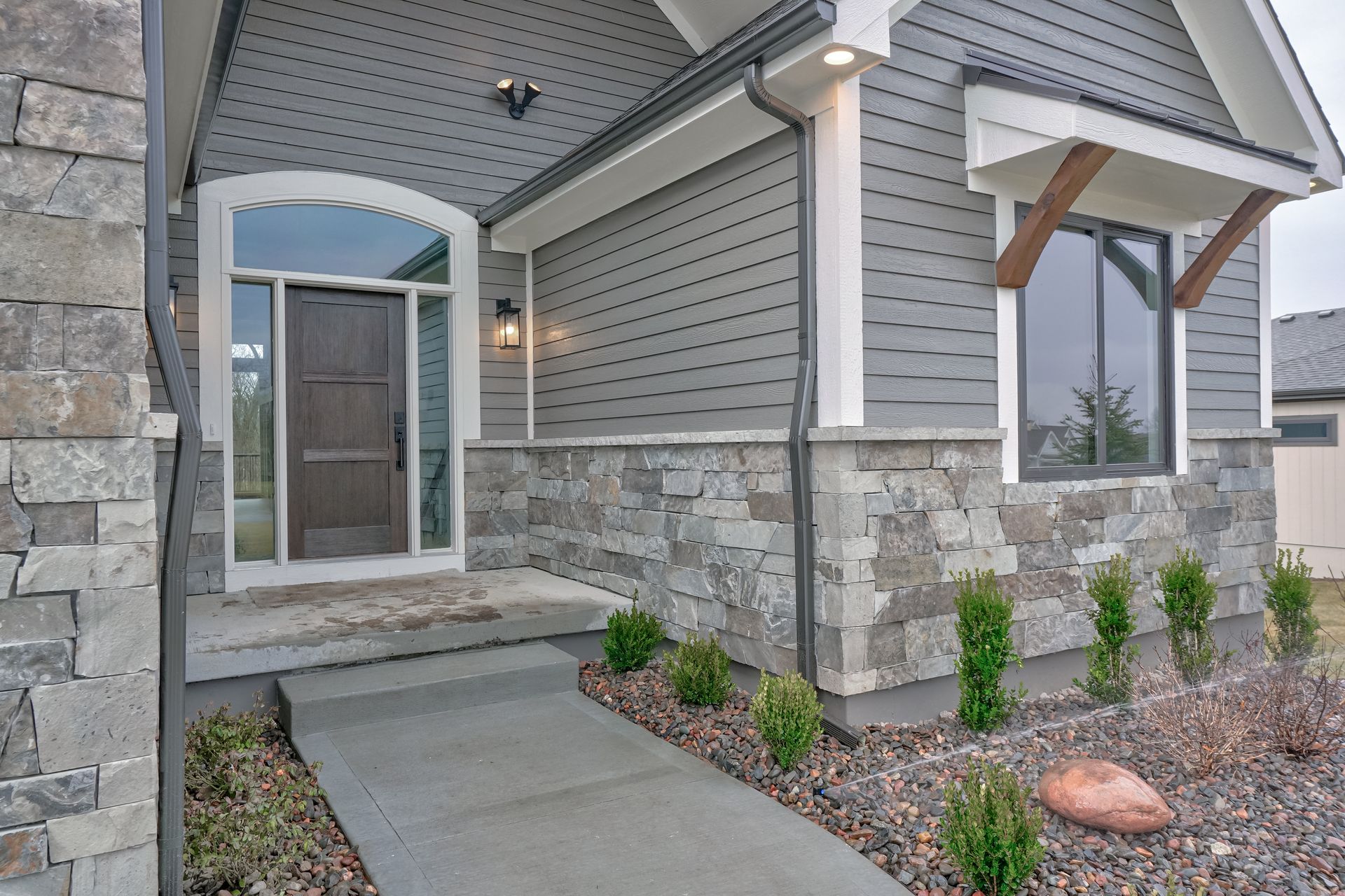 A gray house with a stone wall and a walkway leading to the front door