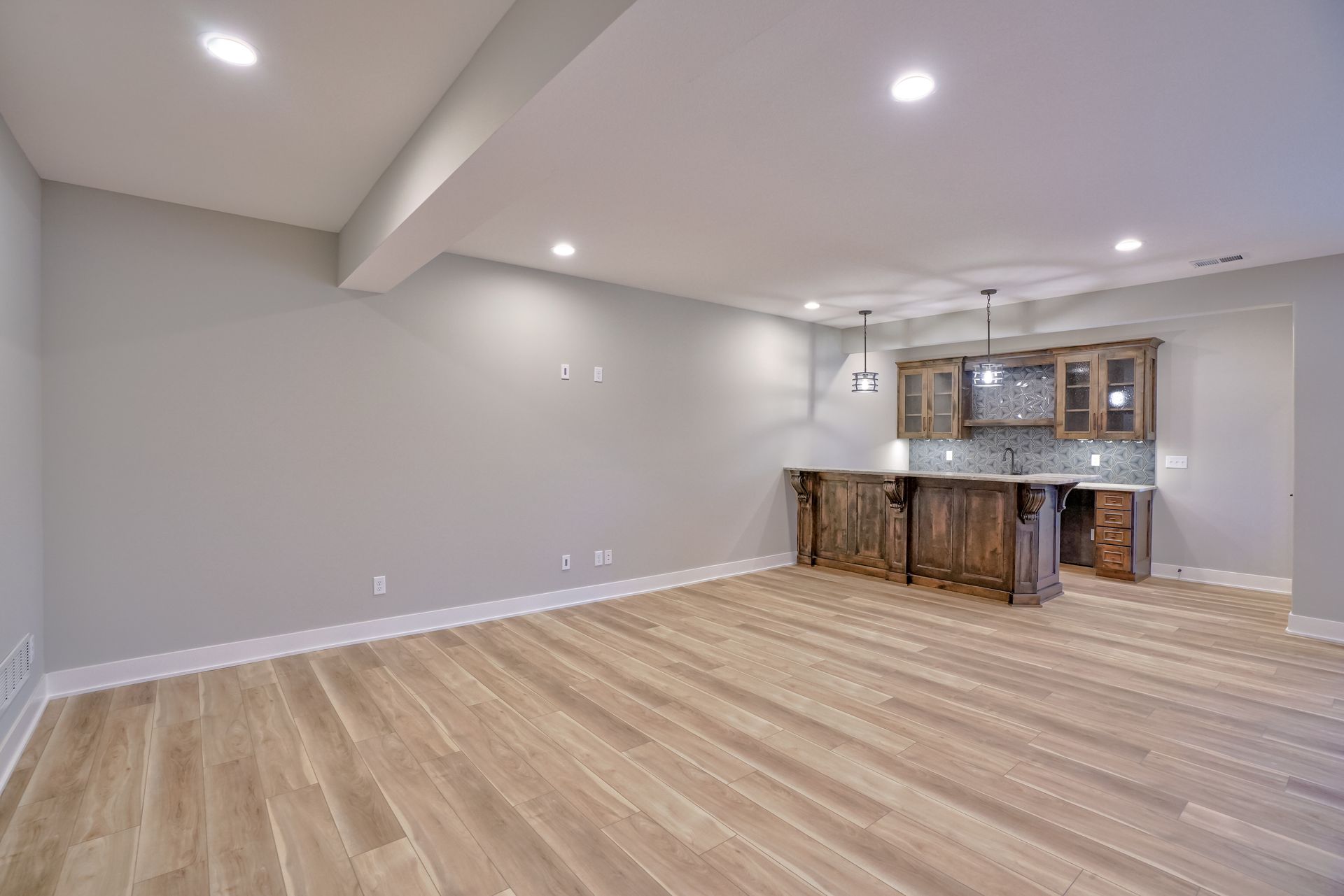 An empty basement with hardwood floors and a bar.
