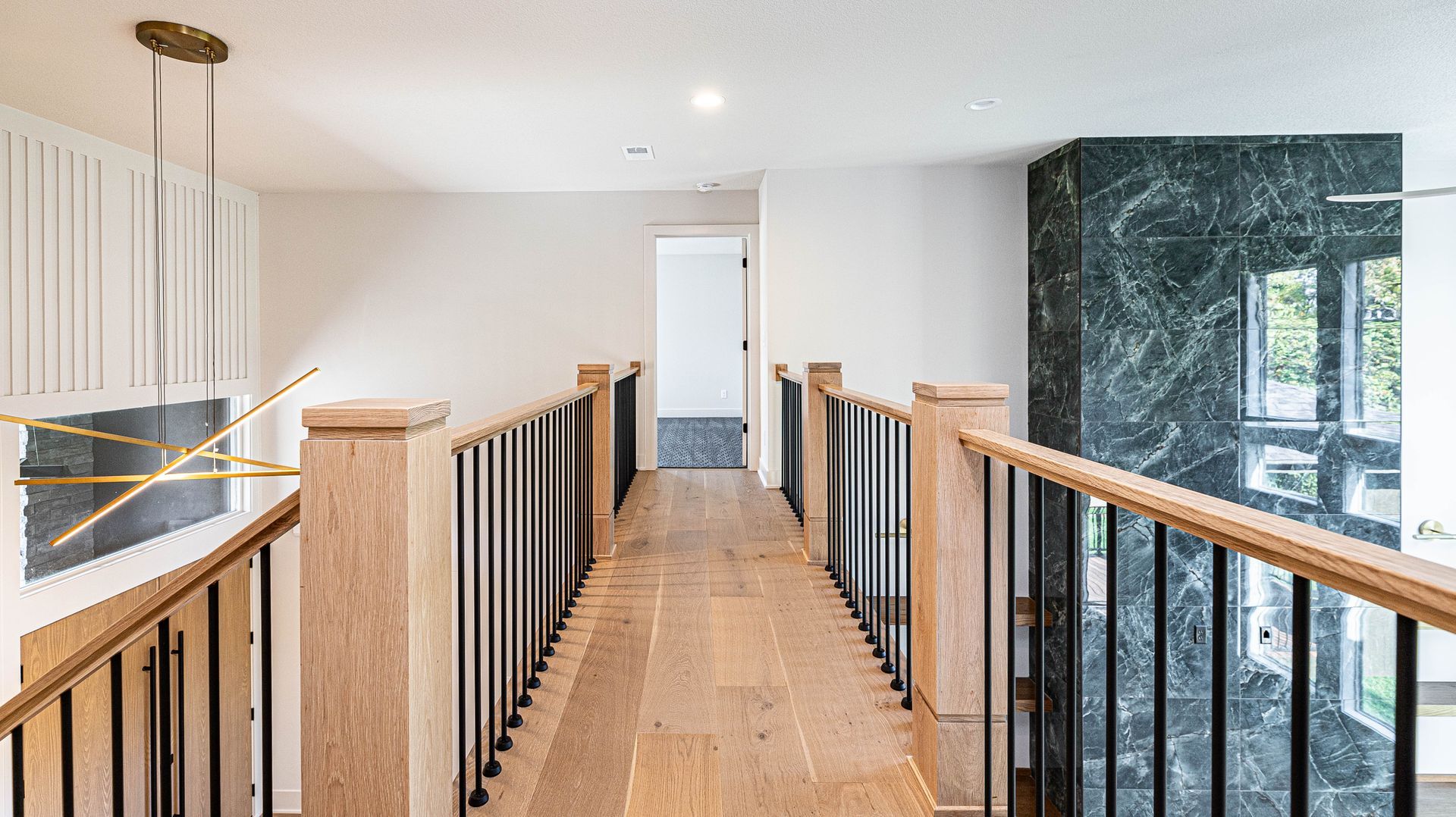 A long hallway with wooden floors and black railings in a house.