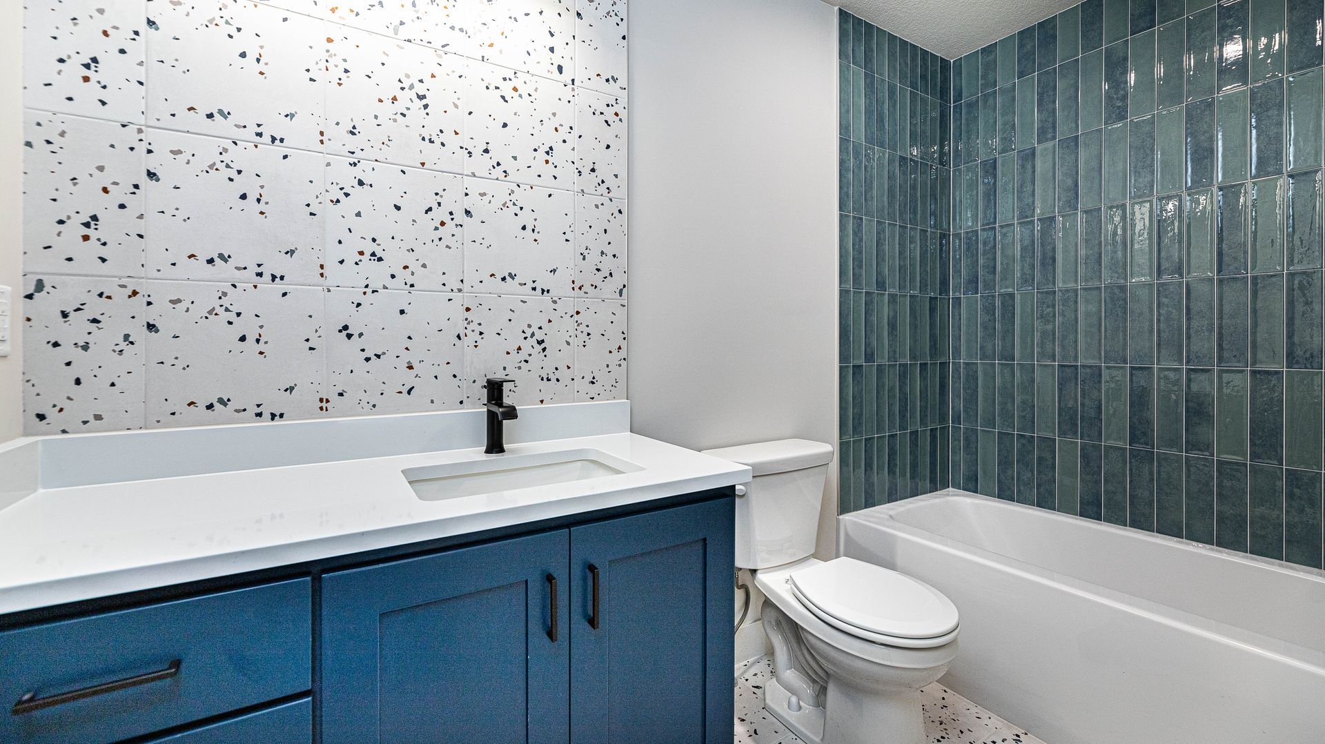 A bathroom with blue cabinets , a toilet , and a bathtub.
