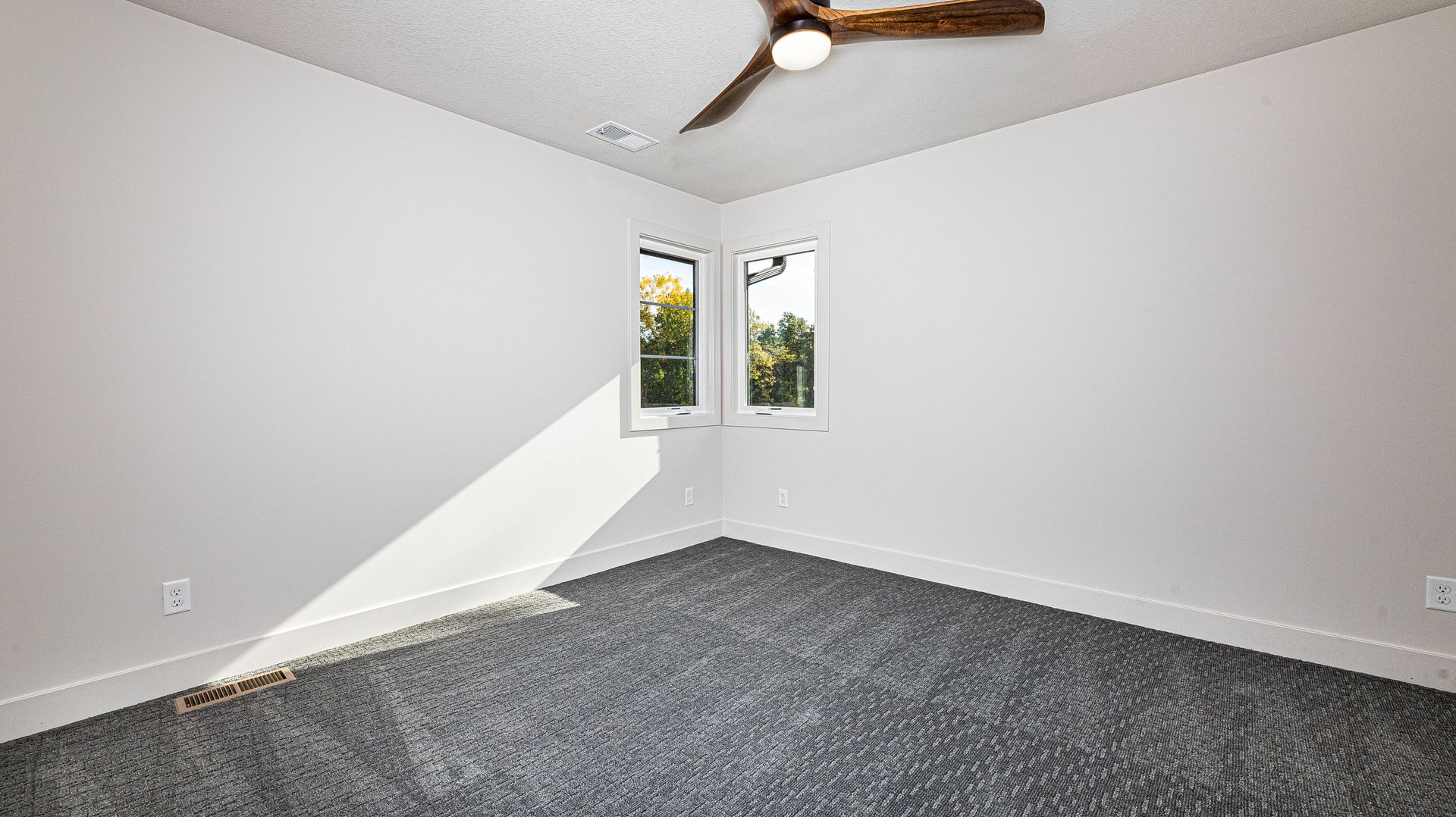 An empty bedroom with a ceiling fan and two windows.