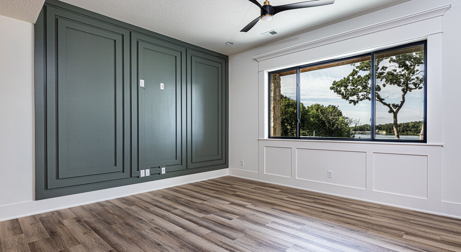 An empty room with a large window and a ceiling fan.