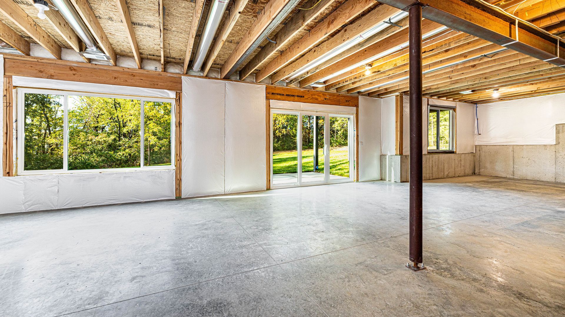 An empty basement with a concrete floor and wooden beams.