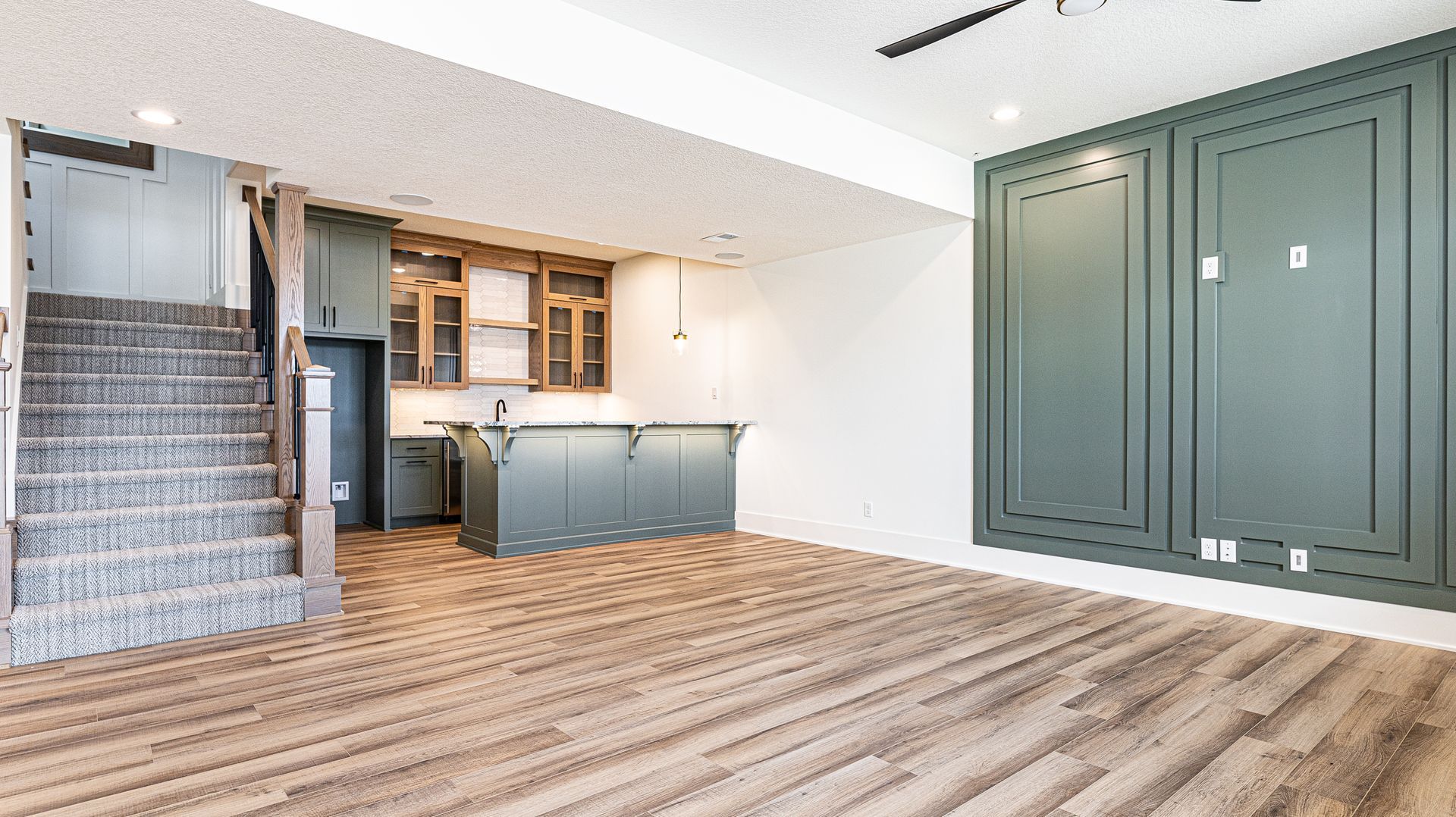 An empty basement with hardwood floors , stairs , and a kitchen.