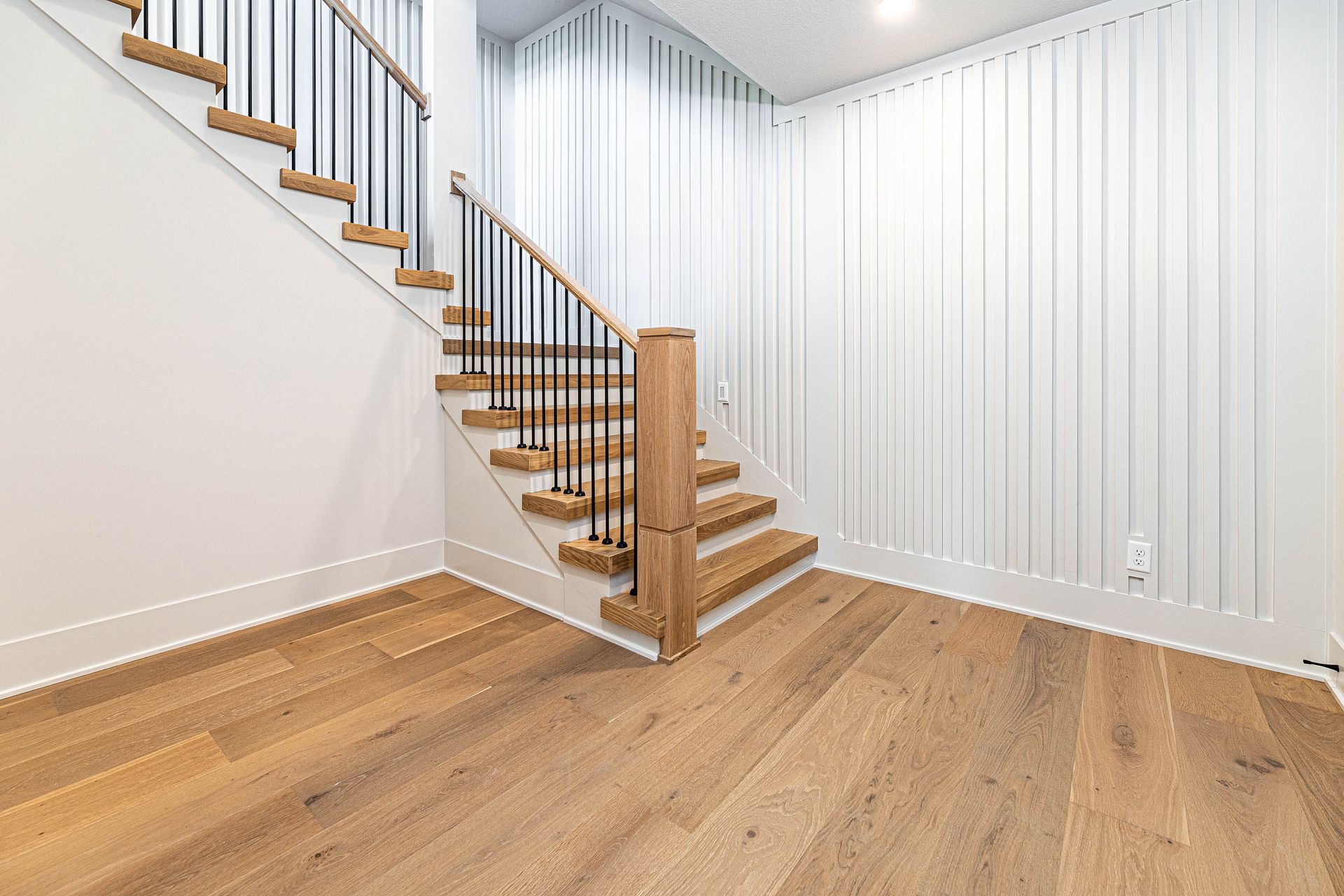 An empty room with a wooden staircase and hardwood floors.