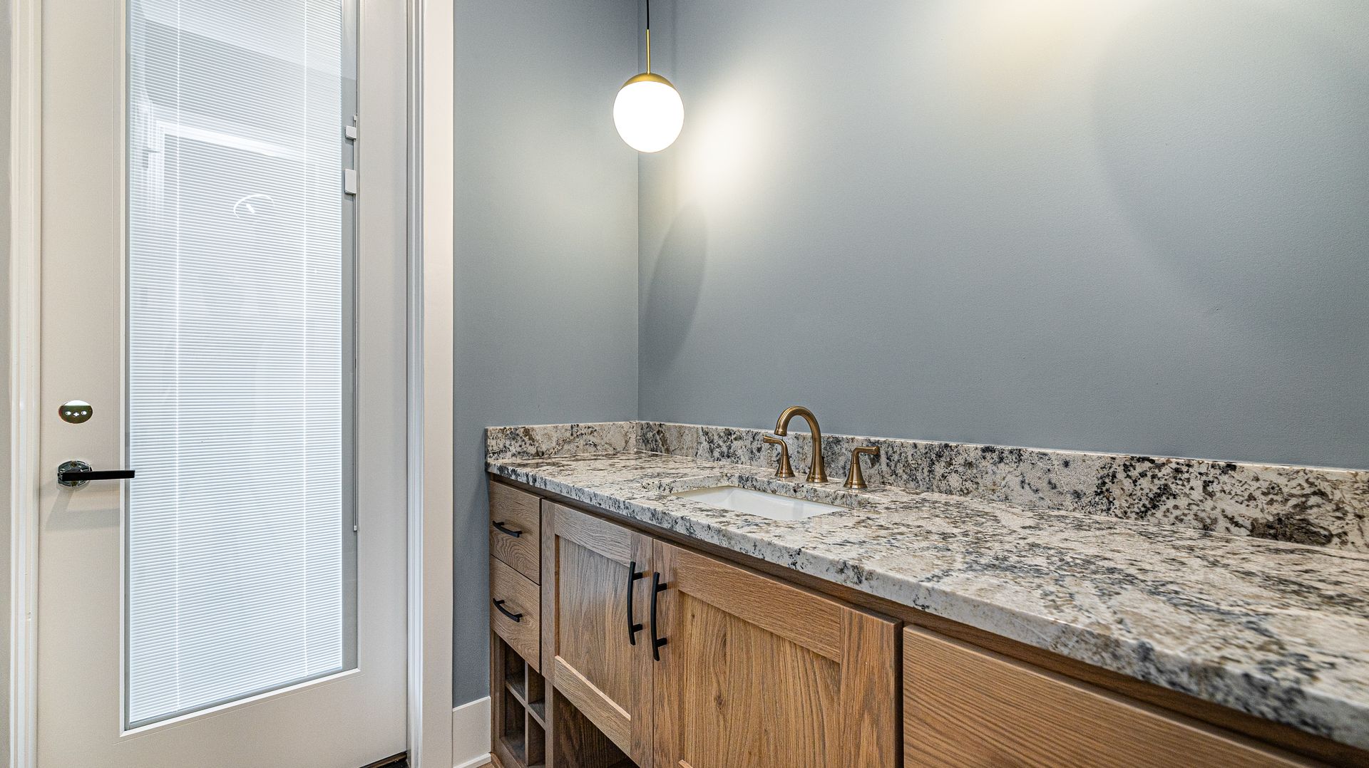 A bathroom with a sink , cabinets and a glass door.