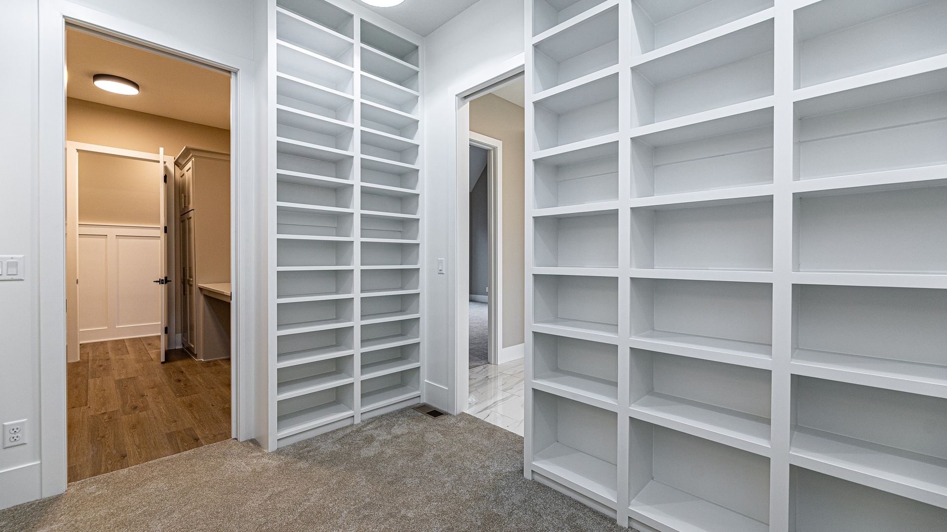 A walk in closet with lots of shelves and a bathroom in the background.