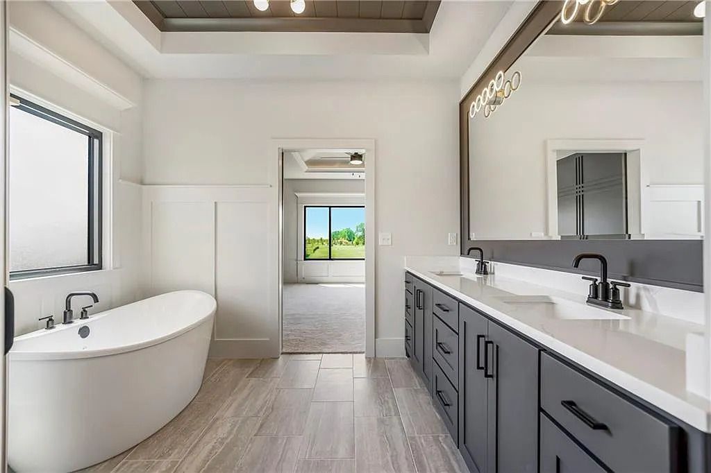 Modern bathroom with a freestanding tub, dark gray vanity, and view into a bedroom.