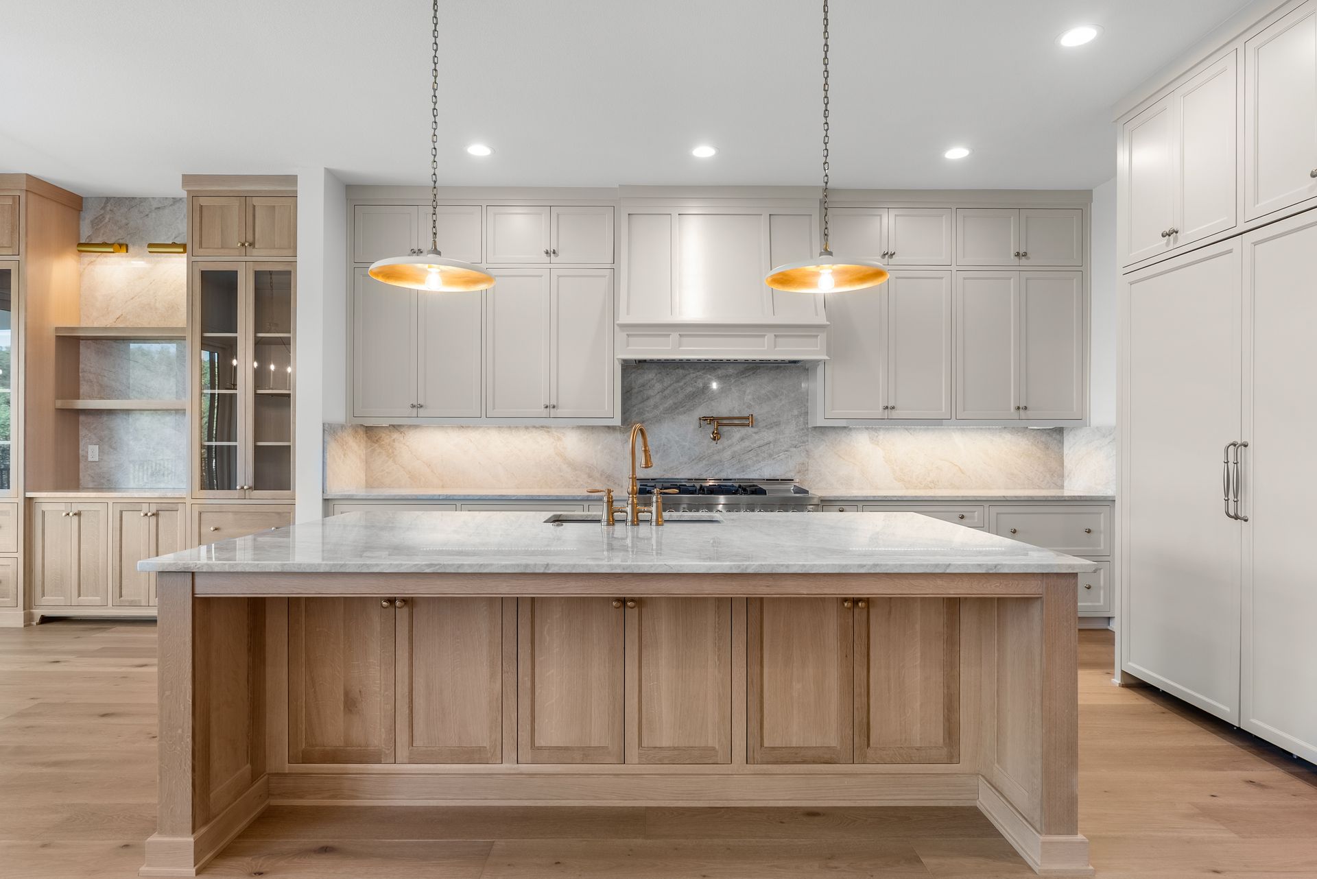 Modern kitchen with light wood cabinetry, marble countertops, and island.