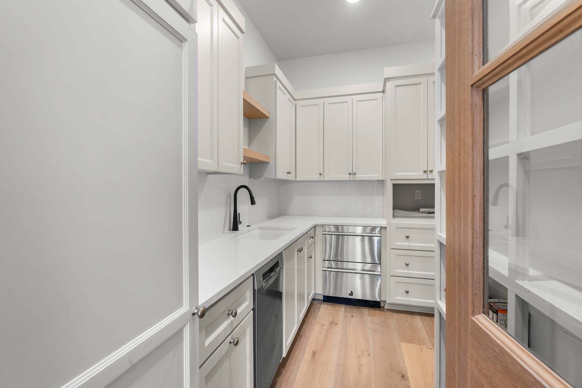 Narrow kitchen with white cabinets, stainless steel appliances, and light wood floors.