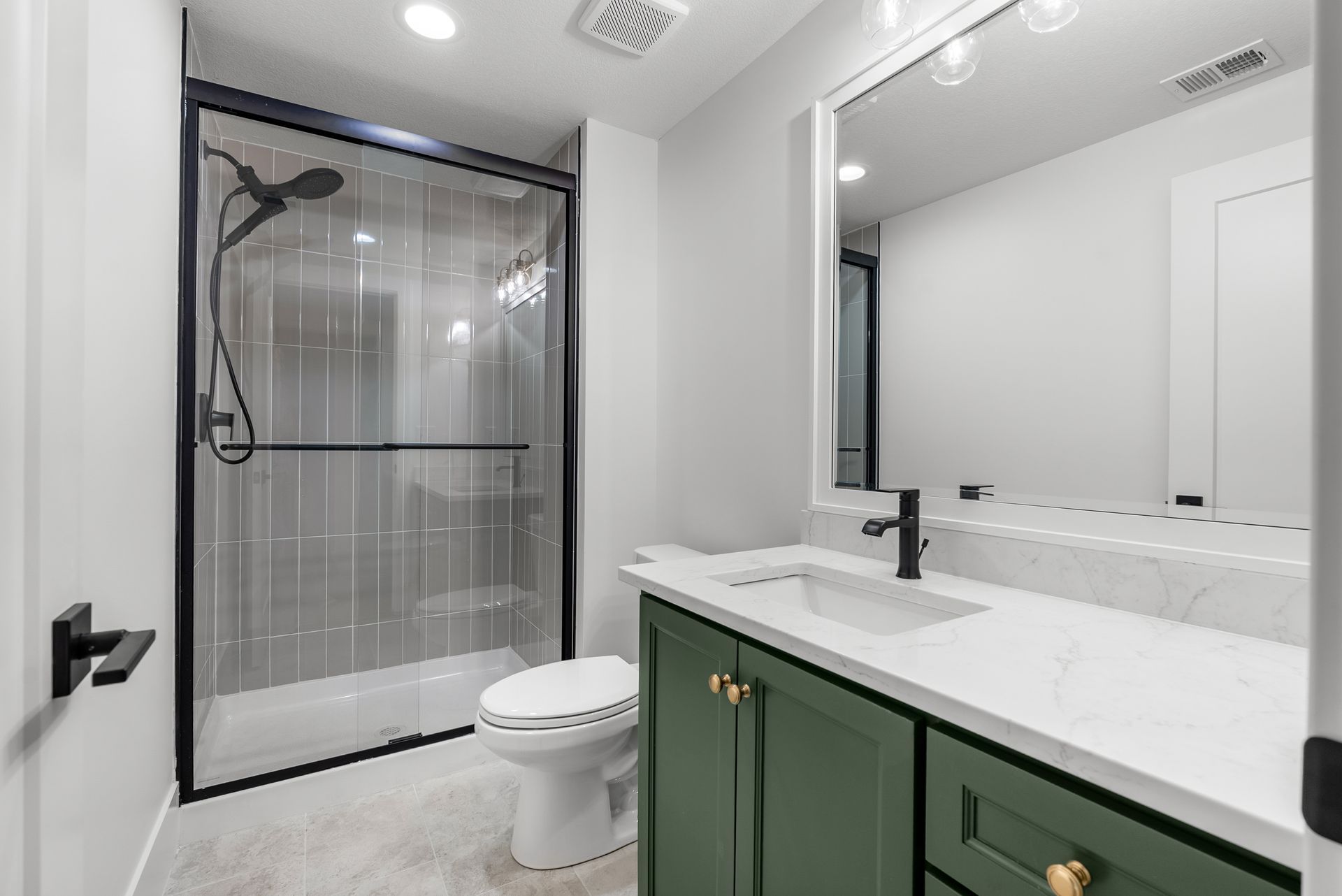 Modern bathroom with green vanity, white countertop, glass shower, and black fixtures.