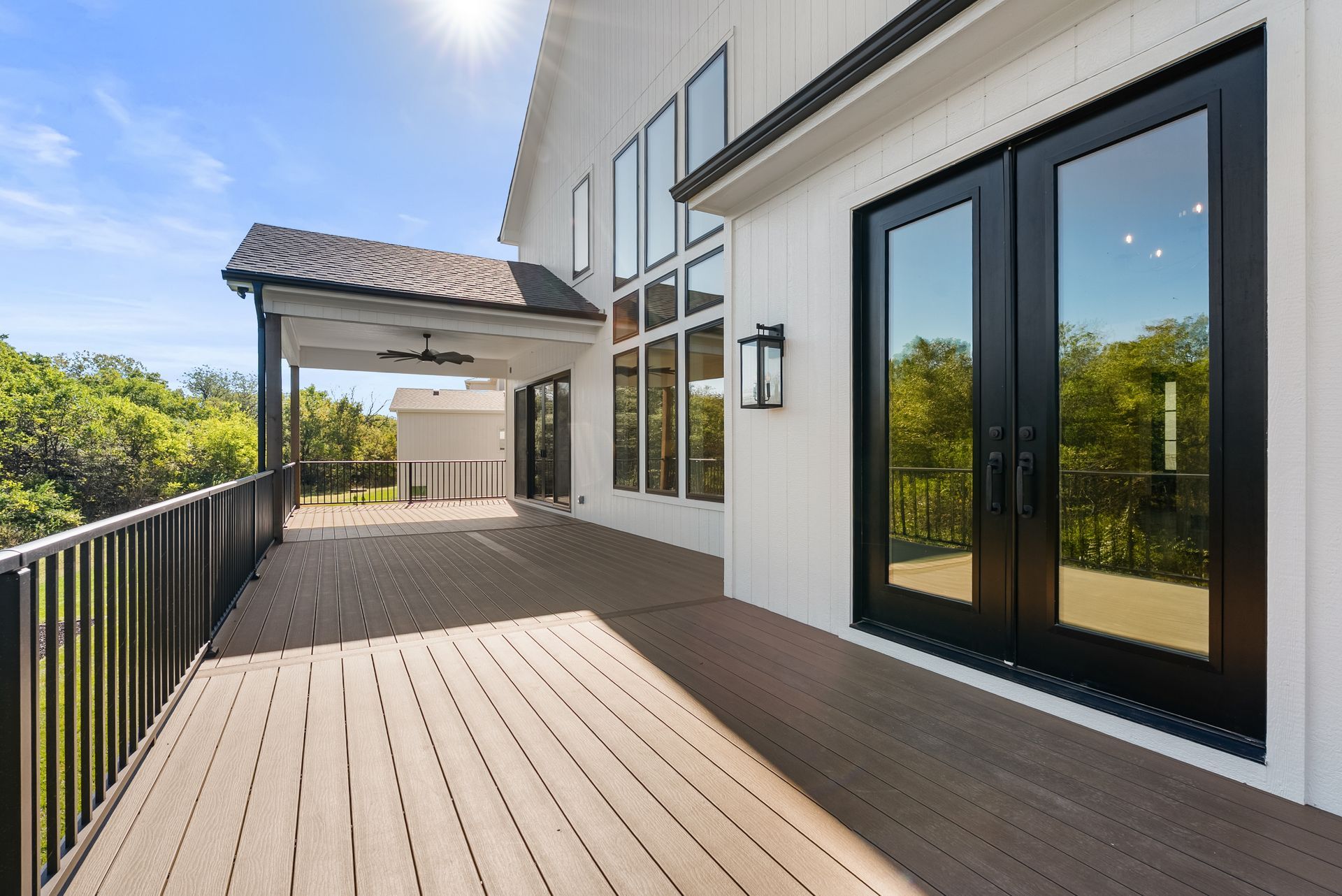 Exterior deck with black doors and railing; white siding; sunny day.