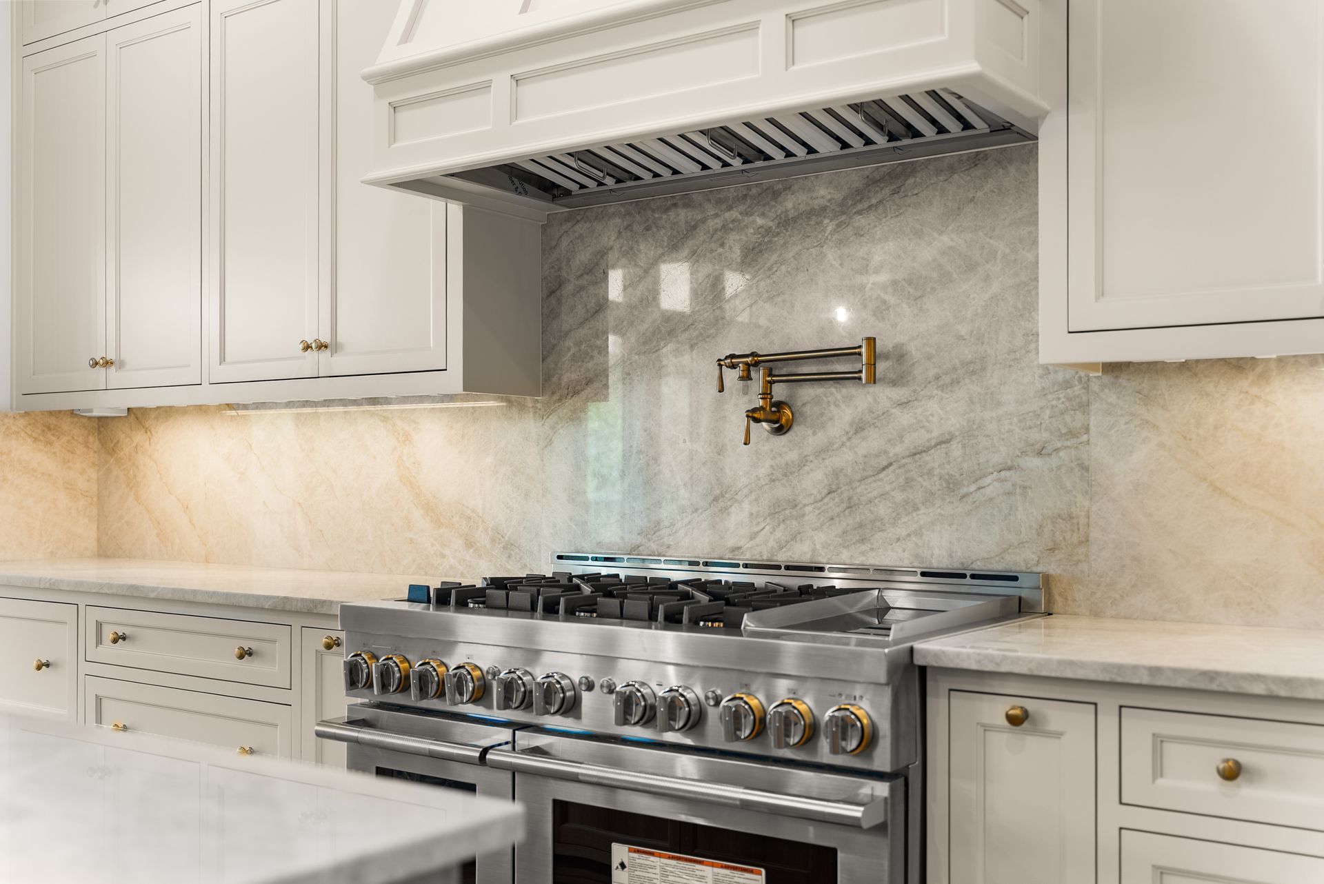 Kitchen with a stainless steel range, marble backsplash, and white cabinets.