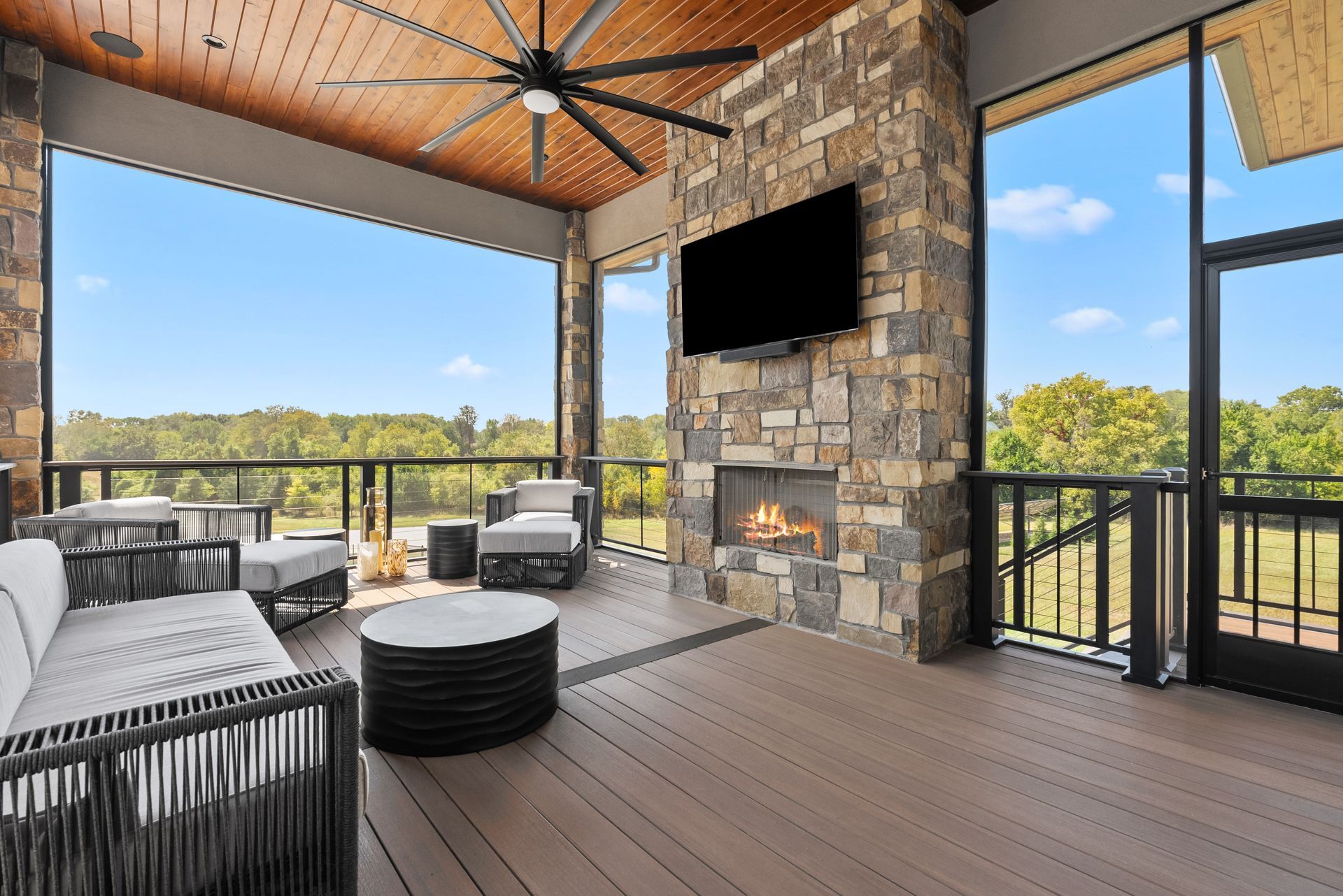 Outdoor patio with a fireplace, TV, seating, and a view of trees and sky.