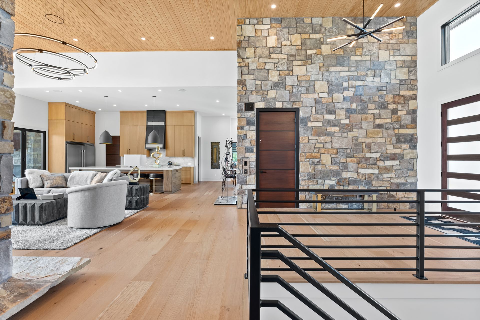 Spacious modern home interior with wood floors, stone accent wall, and open kitchen.