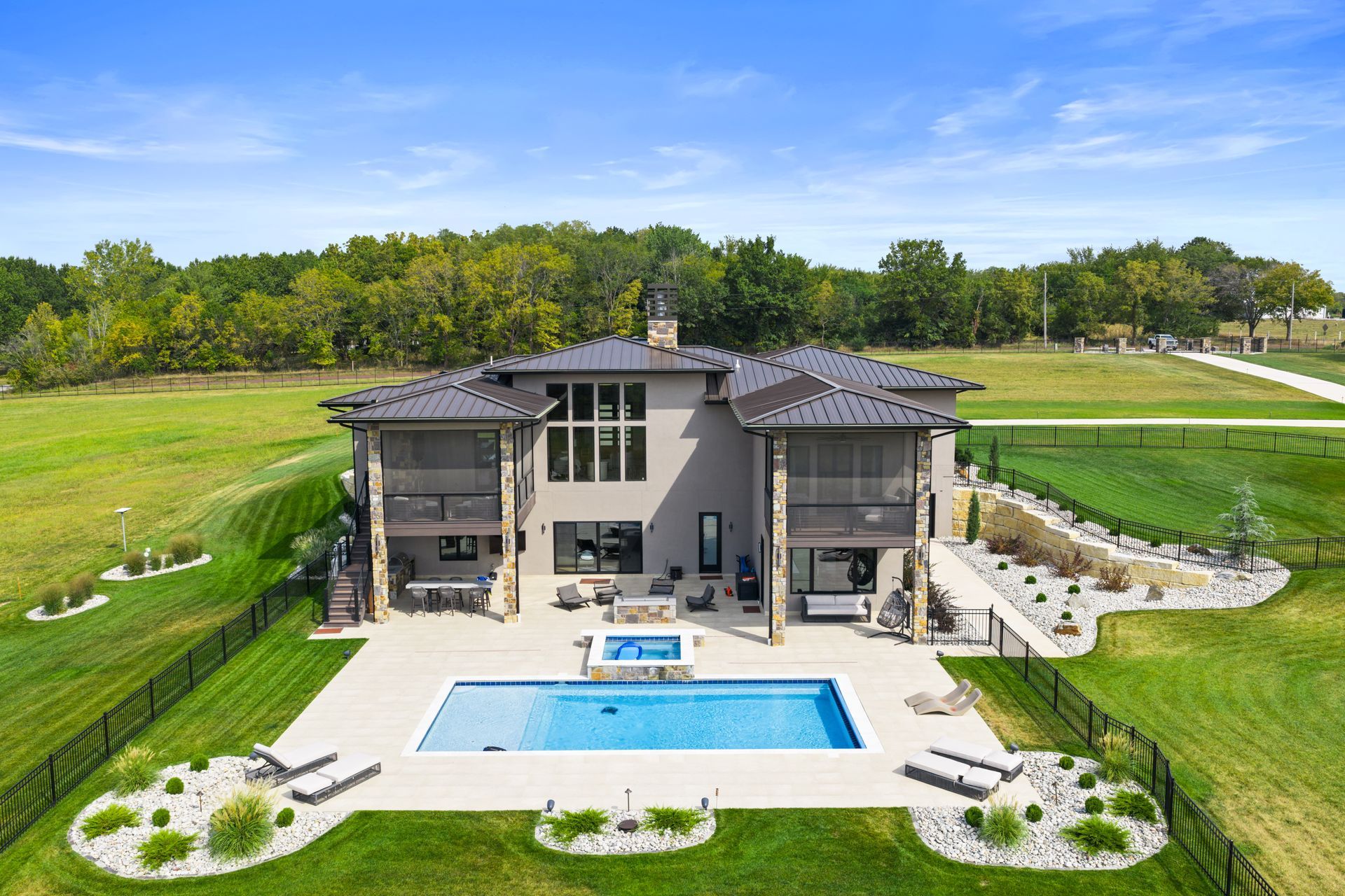Luxury home with pool, patio, and manicured lawn, set against a backdrop of green fields and trees.