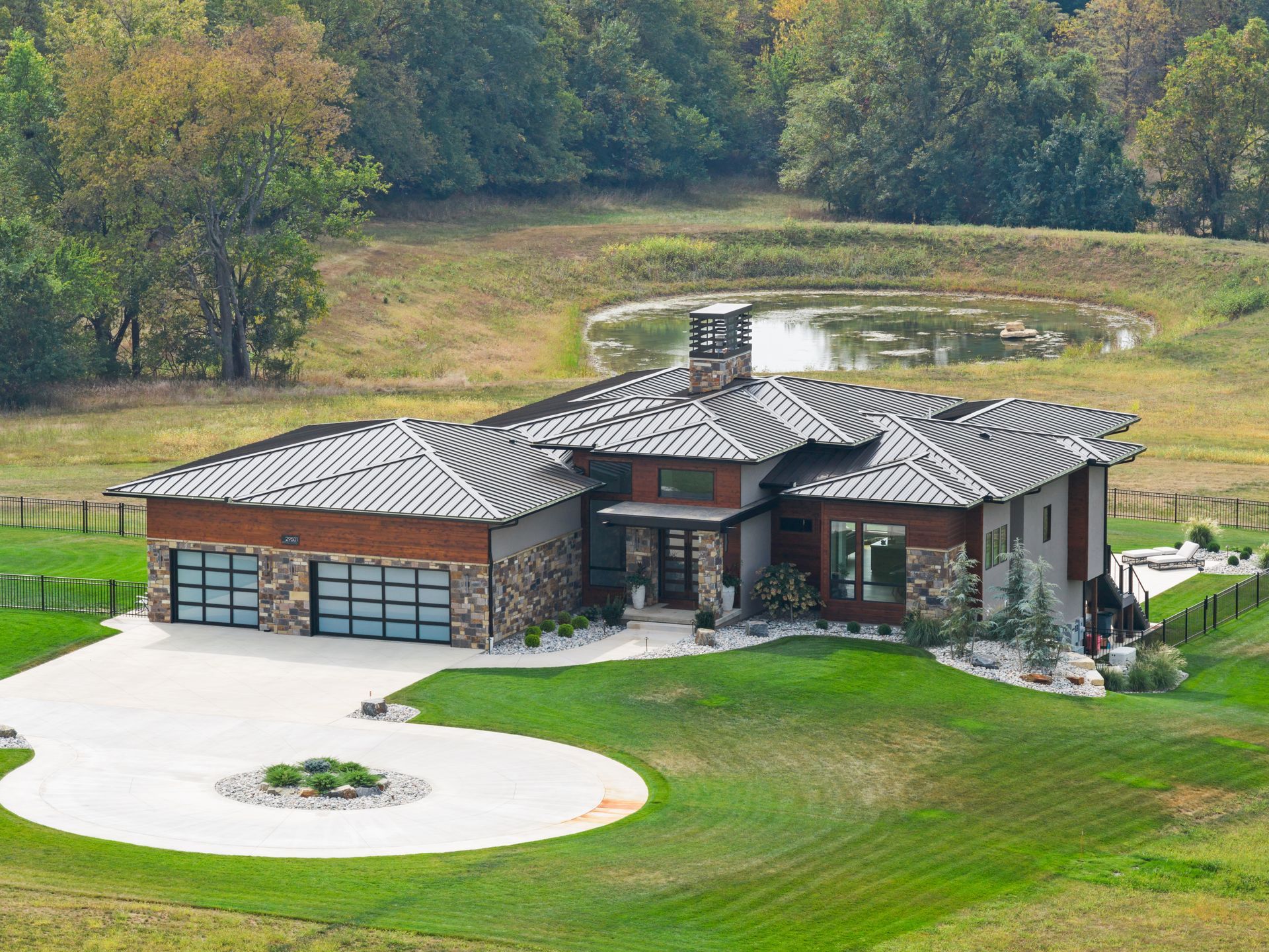 Modern home with stone and wood accents, overlooking a pond on a grassy hill.