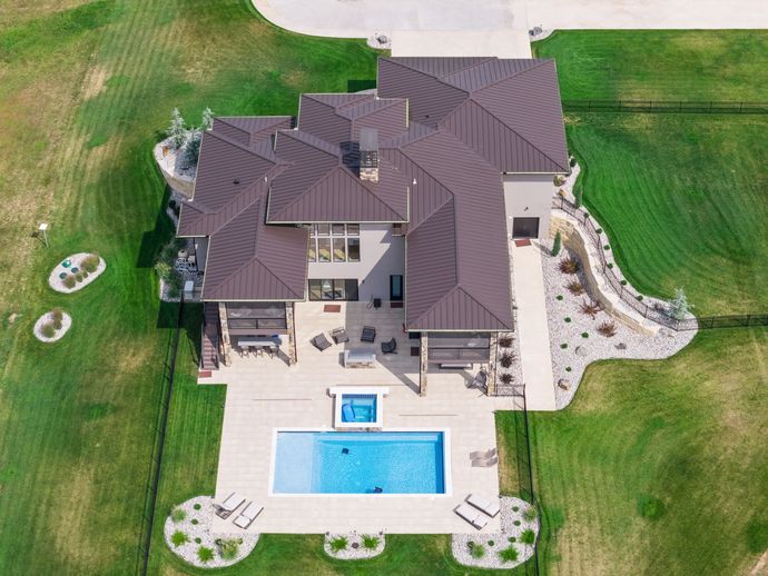 Aerial view of a luxury home with a pool, patio, and manicured landscaping on a large grassy lot.
