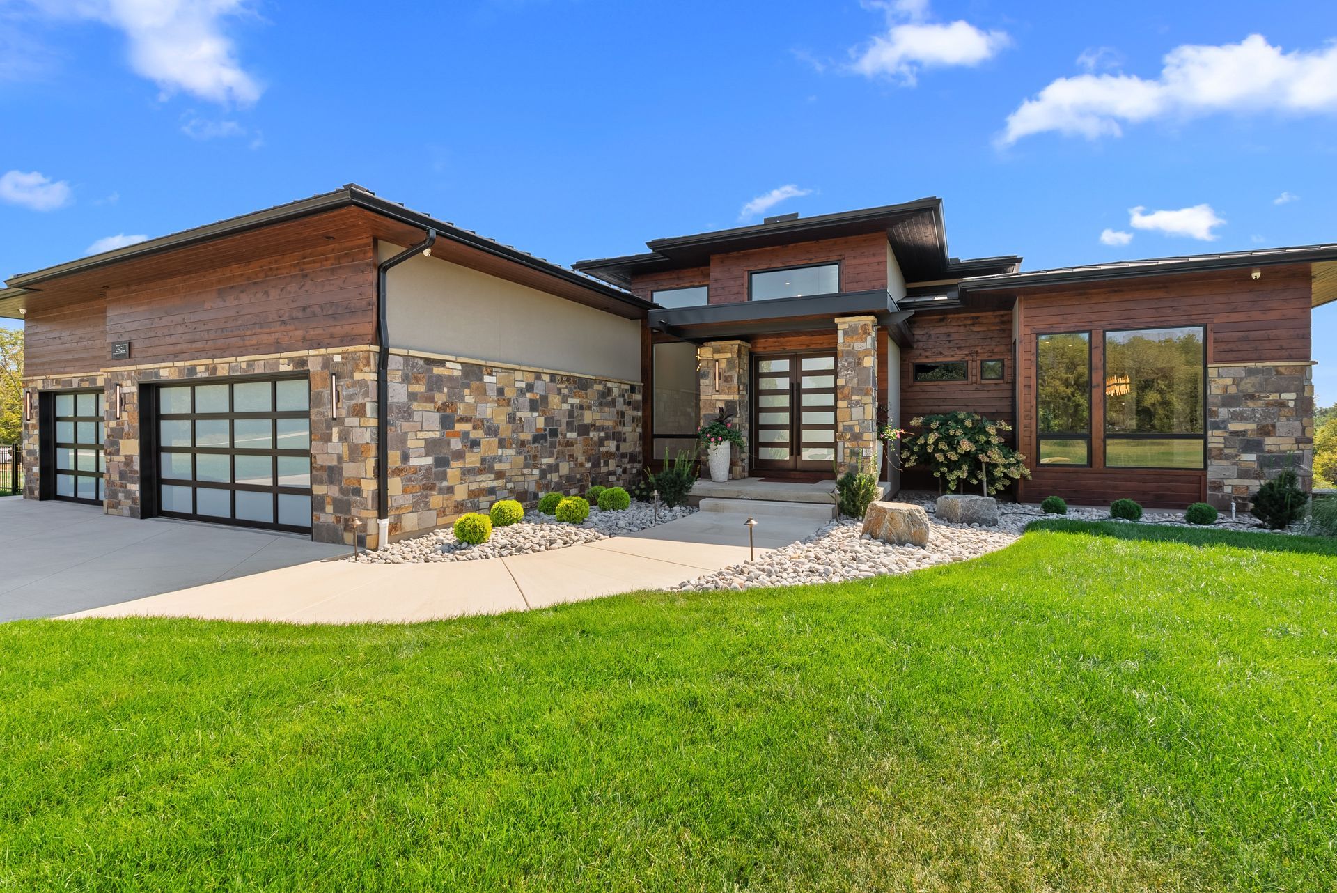 Modern home with a brick exterior, stone accents, and glass garage doors; green lawn and blue sky.