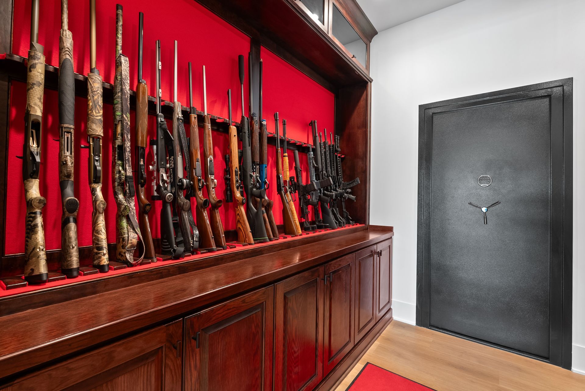 Guns displayed in a red-lined wooden cabinet; a large, dark safe door is next to them.
