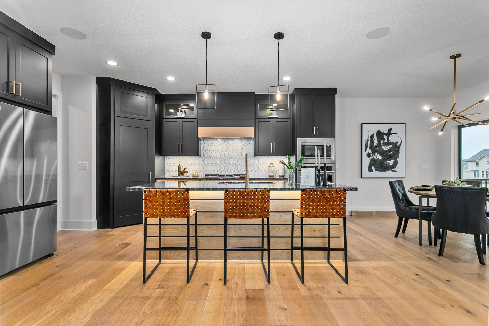 A kitchen with black cabinets , stainless steel appliances , wooden floors and a large island.