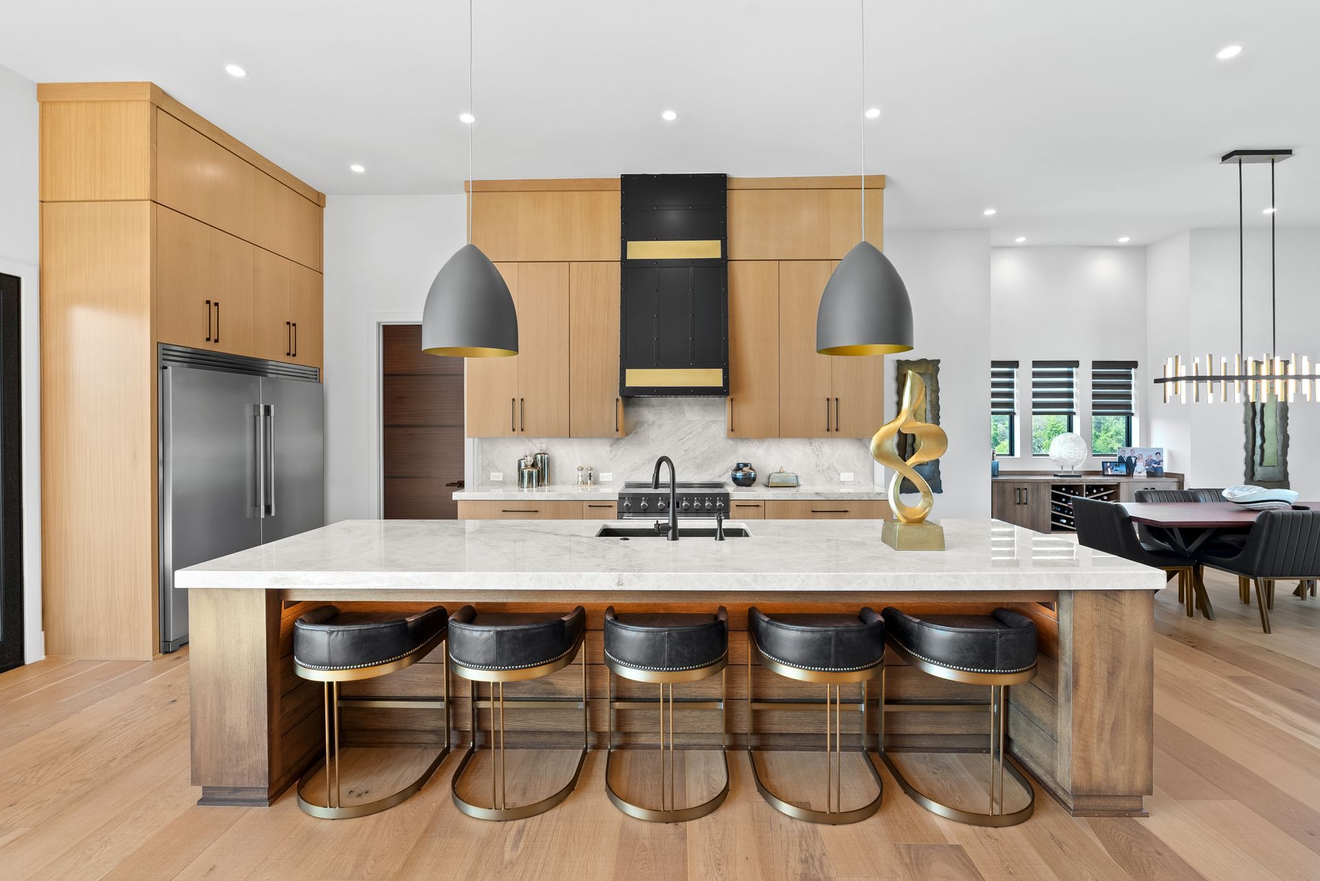 Modern kitchen with island seating, wood cabinetry, black accents, and stainless steel appliances.