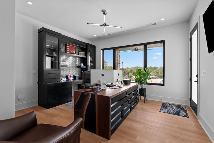 Modern home office with a desk, dark cabinets, large window, and leather chair.