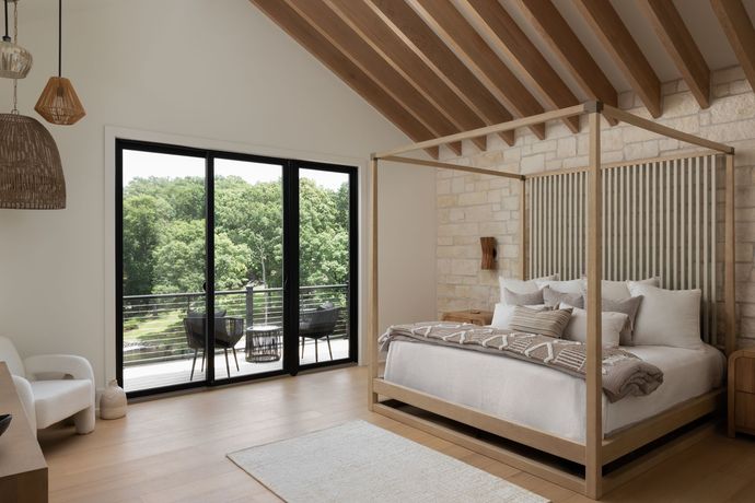 Bedroom with four-poster bed, balcony, and wooden ceiling beams; light and airy feel.