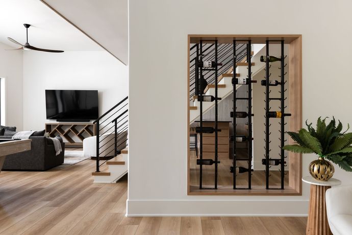 Modern wine rack built into a wall, showcasing bottles. Staircase visible. Bright, minimalist interior.