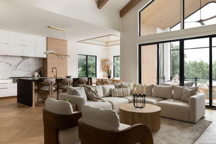 Modern living room with sectional sofa, open kitchen, and large windows overlooking greenery.