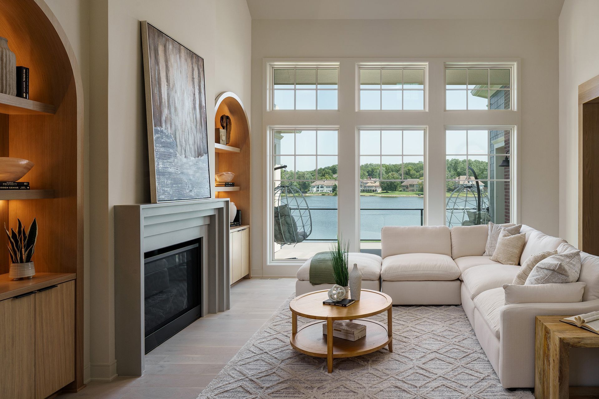 A living room with a couch , fireplace , and lots of windows overlooking a lake.
