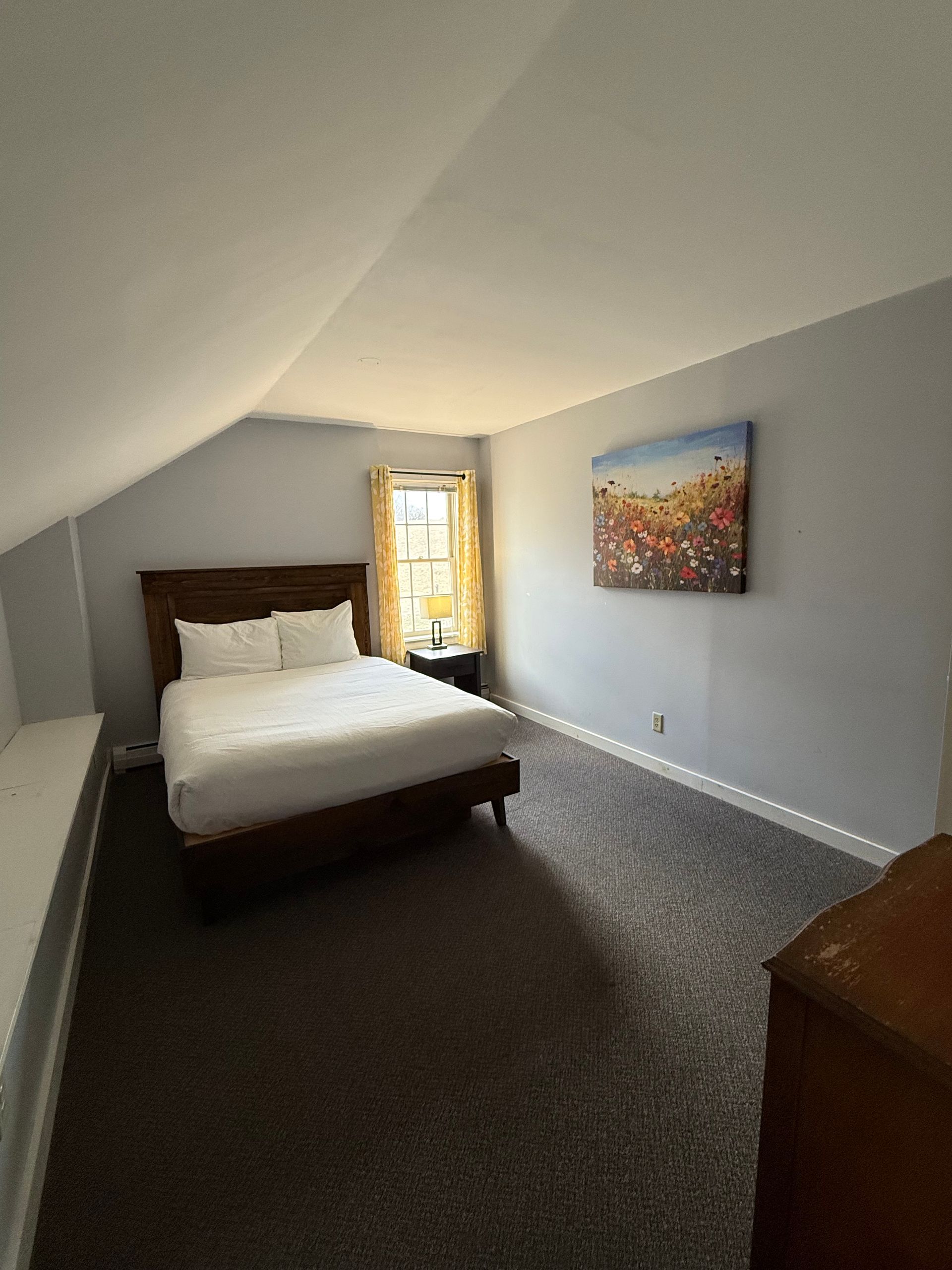 Small bedroom with a bed, gray walls, carpeted floor, and a window at the far end.