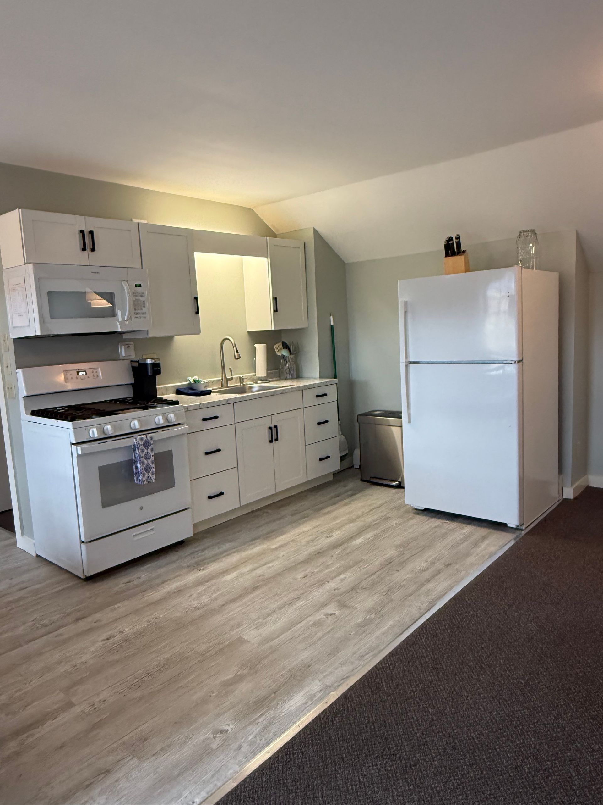 Small kitchen with white cabinets, stove, sink, refrigerator, and light wood flooring