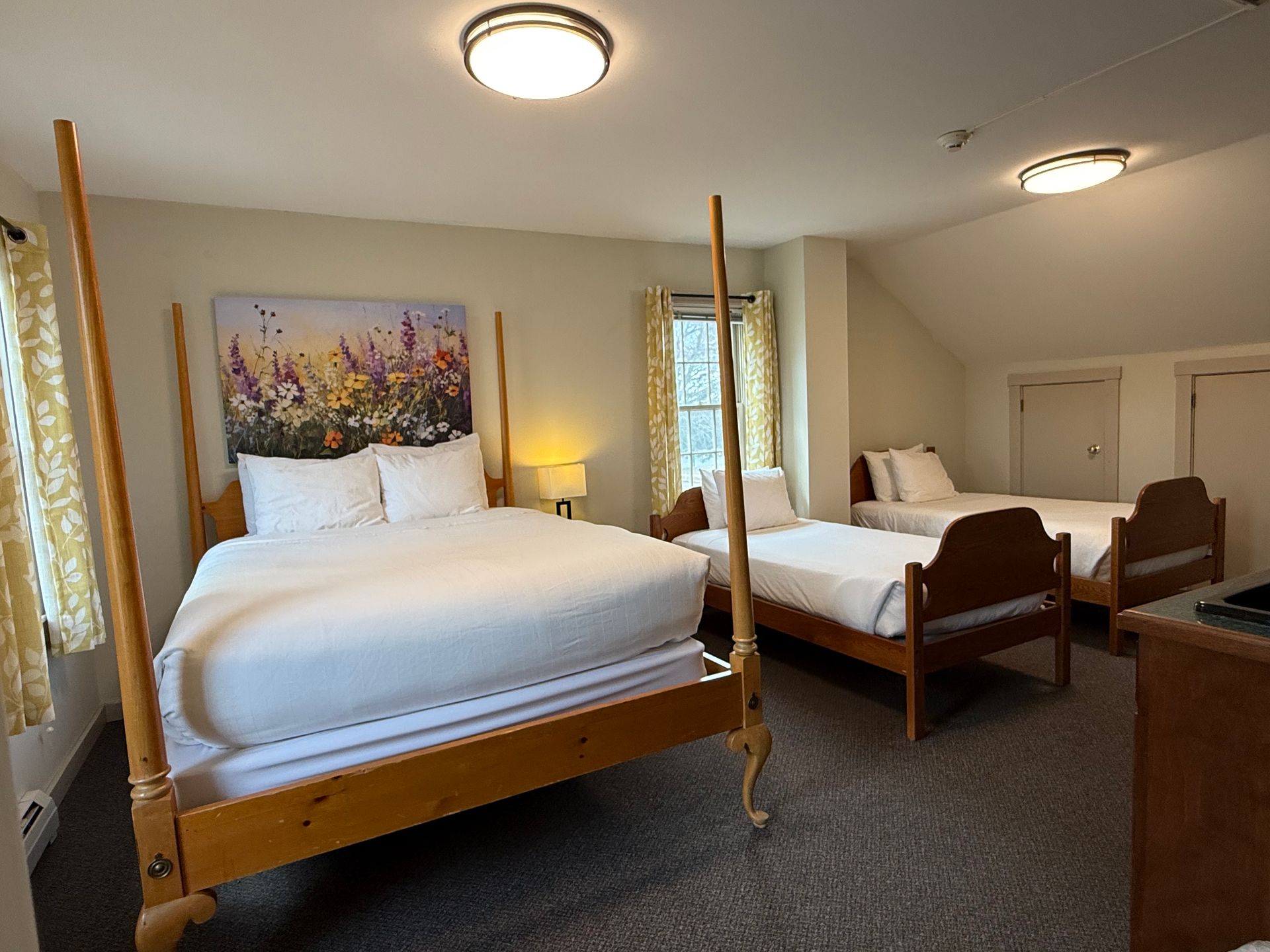 Hotel room with two canopy beds, white bedding, and bedside lamps in a bright, carpeted room