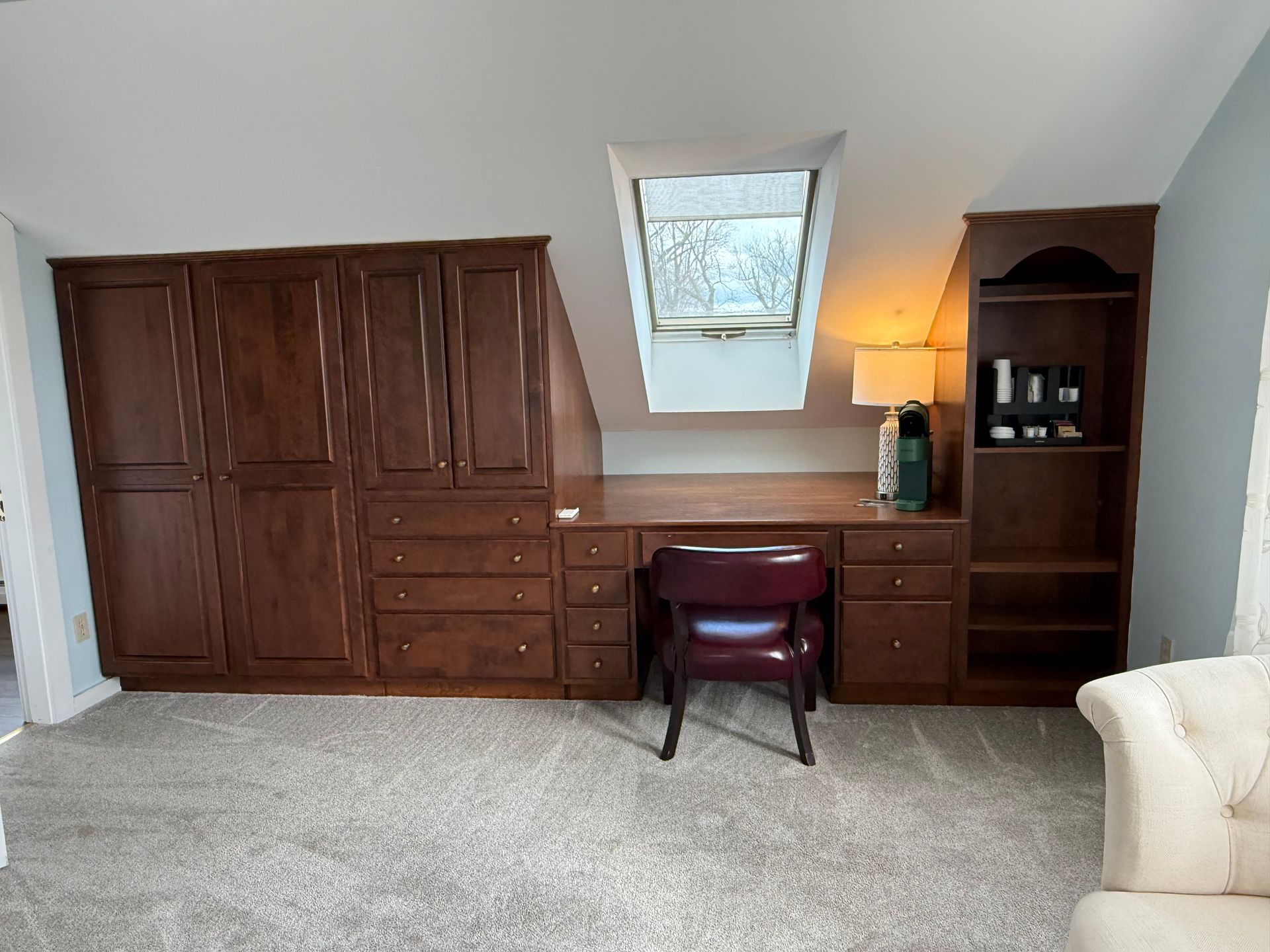 Built-in wood wall unit with desk, drawers, mirror, lamp, and chair in a carpeted room