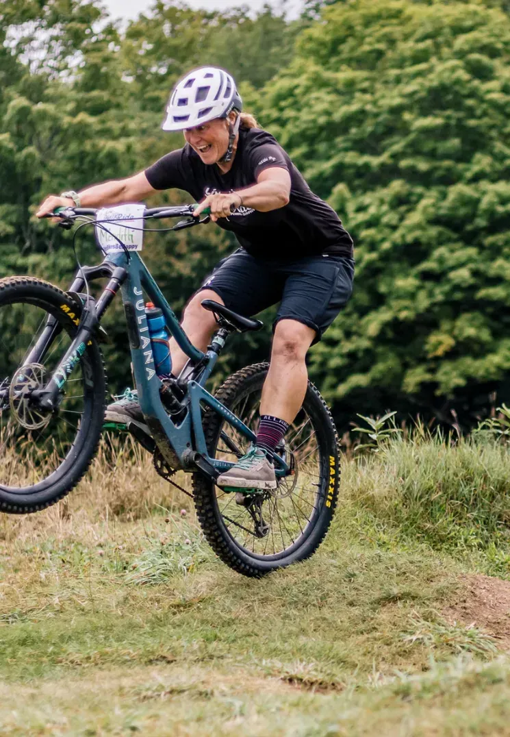 Cyclist in a white helmet performs a wheelie on a mountain bike over grassy terrain.
