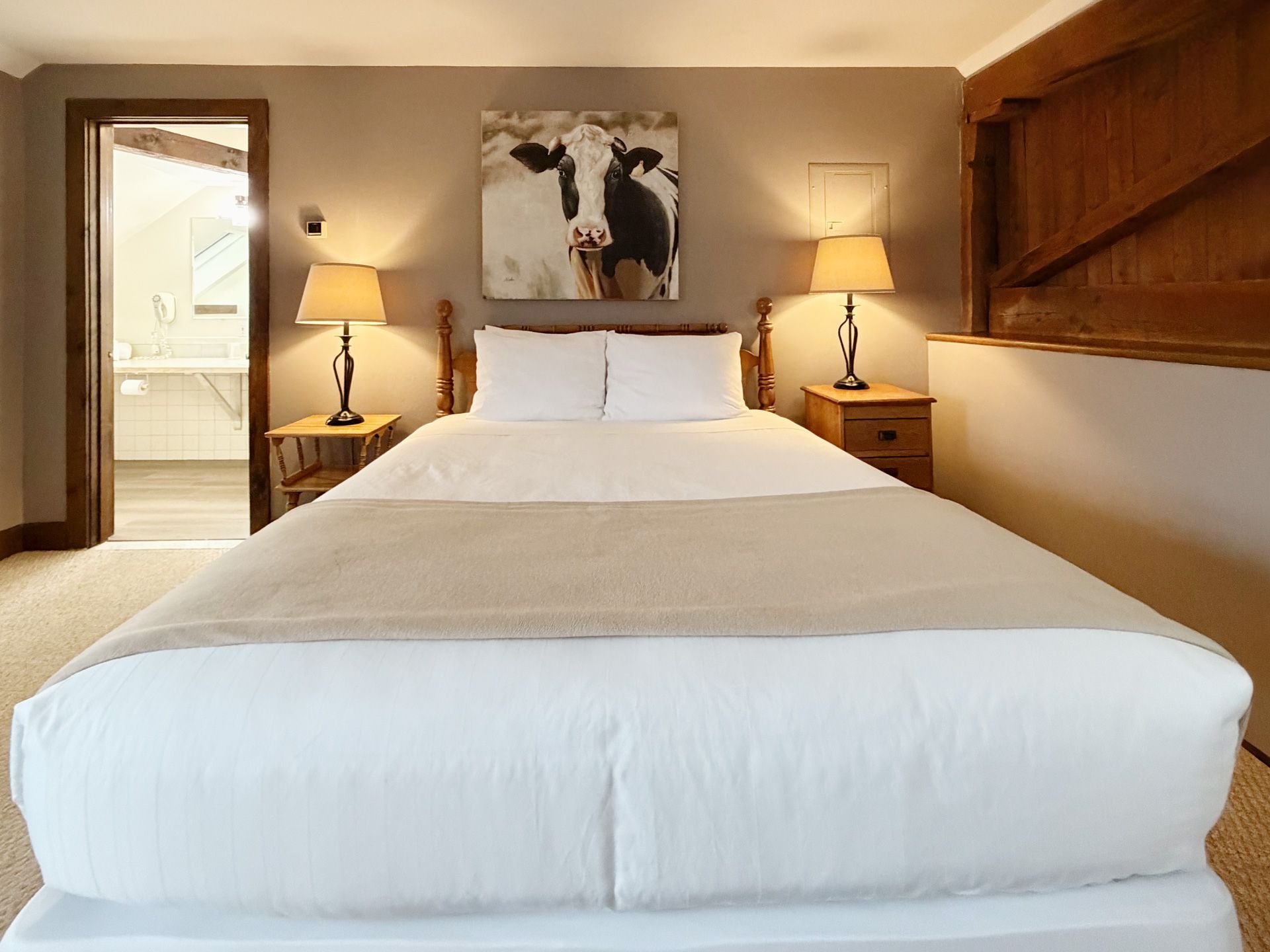 Cozy bedroom with a neatly made bed, bedside lamps, and an open doorway to a bathroom.