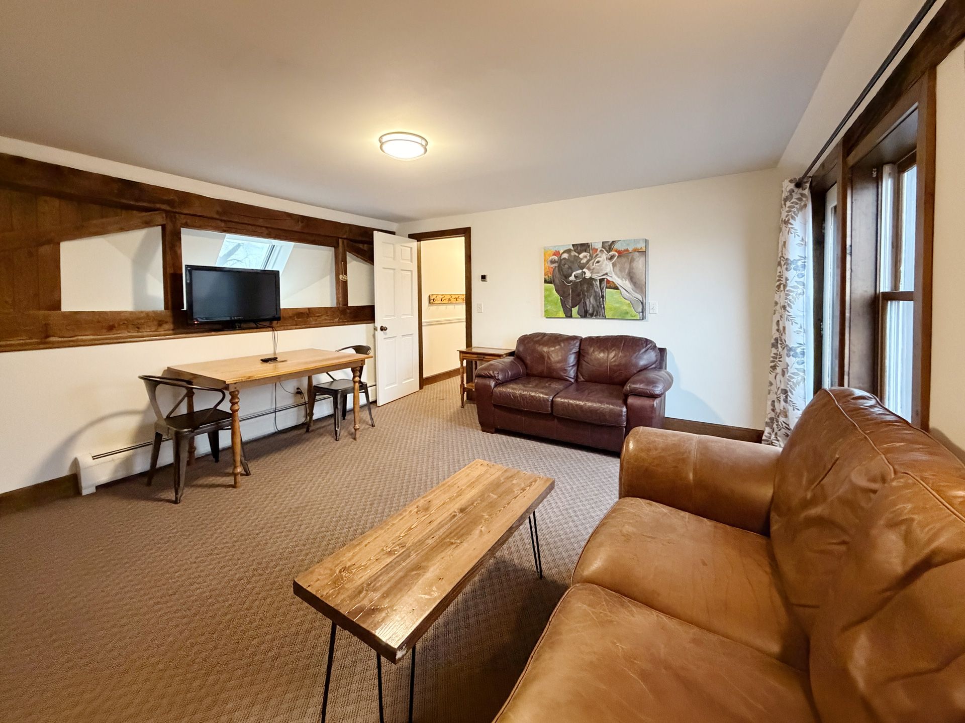Cozy living room with leather sofas, wooden coffee table, TV, wall art, and large windows